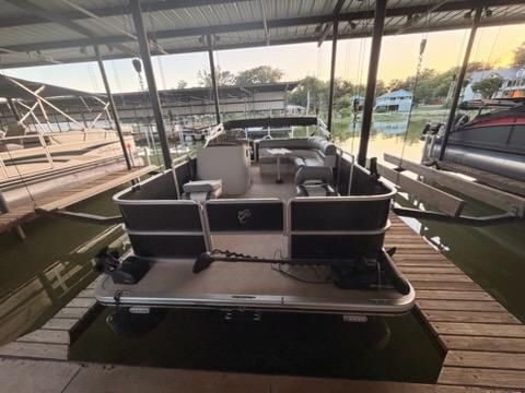 A pontoon boat is docked in a covered slip. It features seating and is surrounded by water.