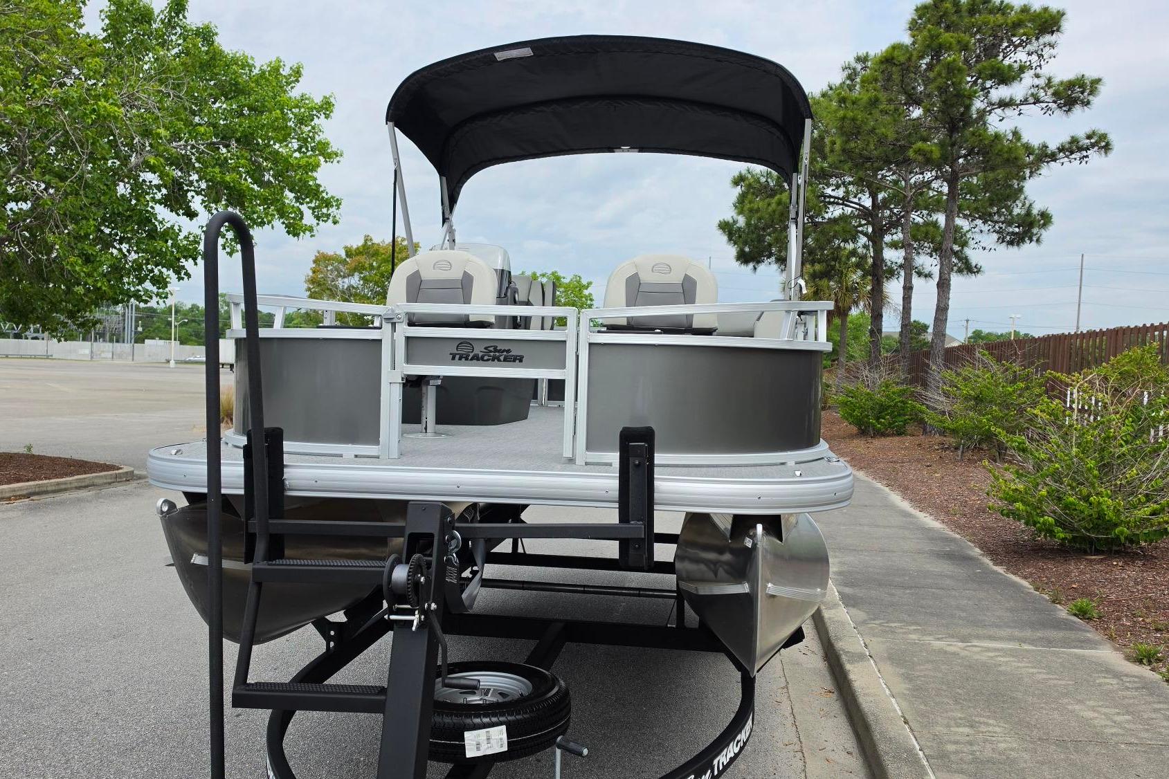 2026 Sun Tracker Bass Buggy 16 XL Select pontoon boat on trailer, parked outdoors.