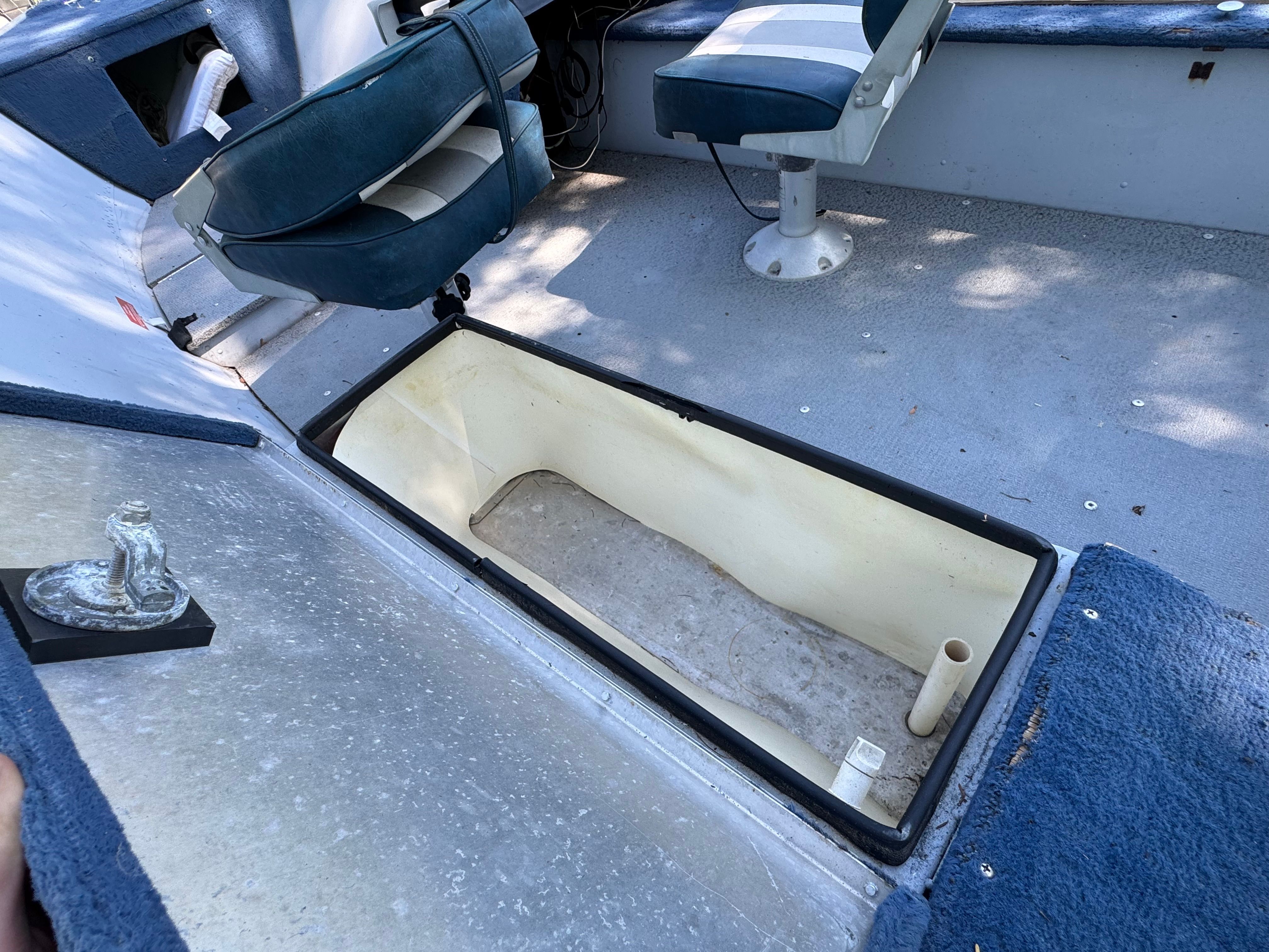 An open storage compartment on a boat with blue seats and a gray floor.
