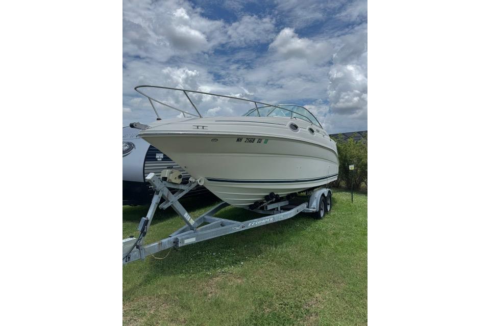 2004 Sea Ray 240 Sundancer boat on trailer, parked on grass under cloudy sky.