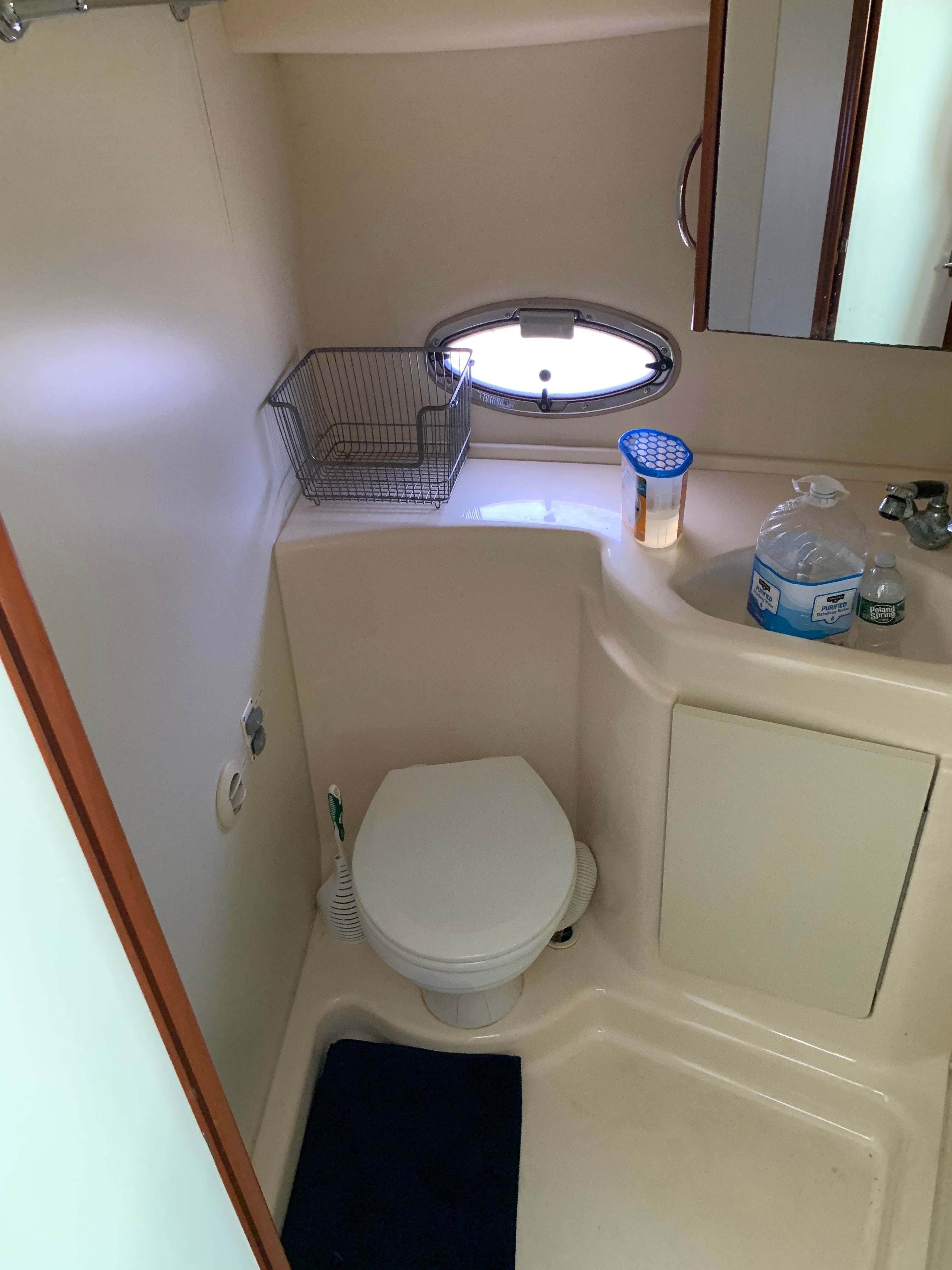 A bathroom on a boat with a toilet, sink, and small window.