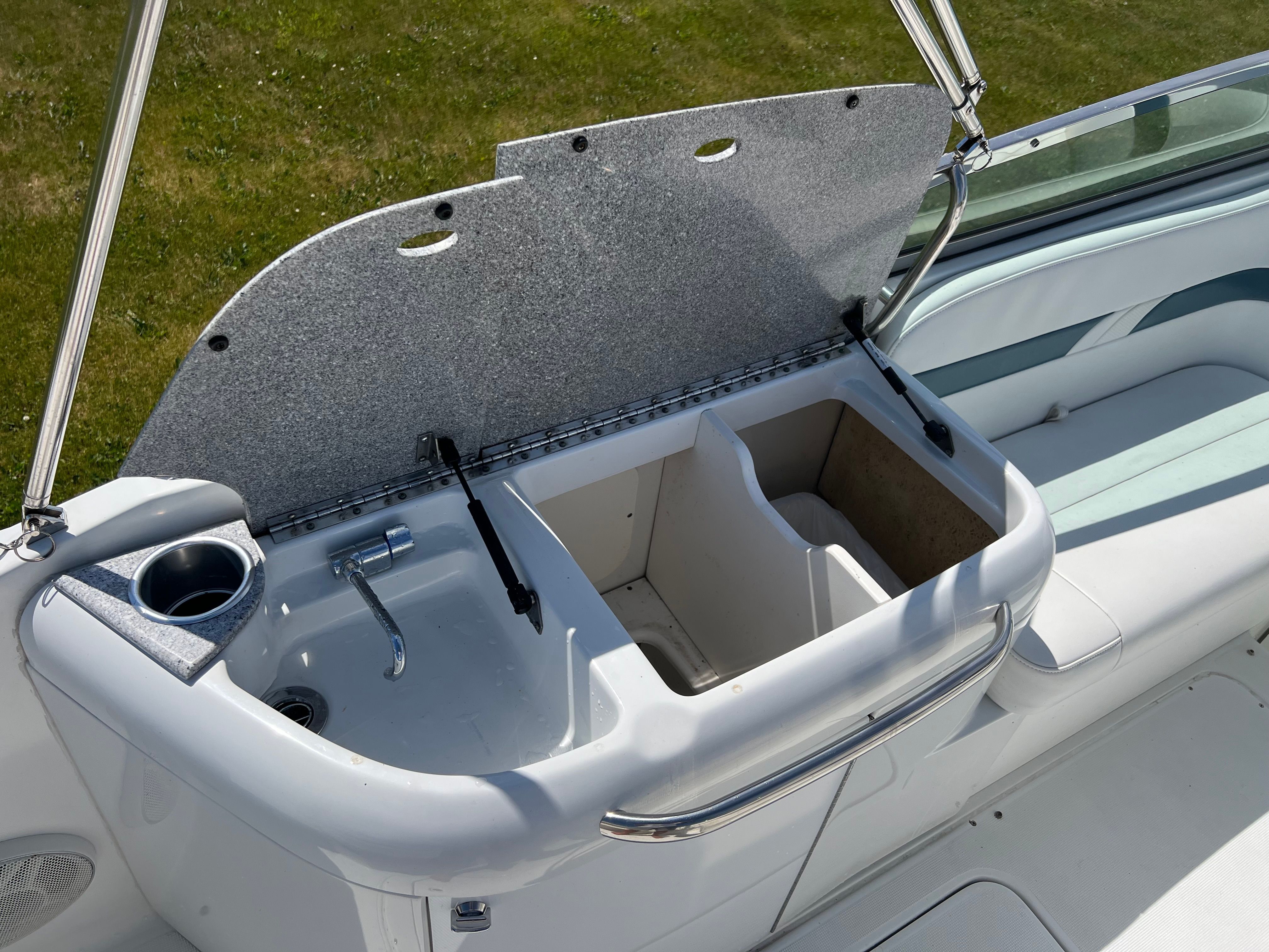 The image shows an open sink with storage on a boat, surrounded by white upholstery.