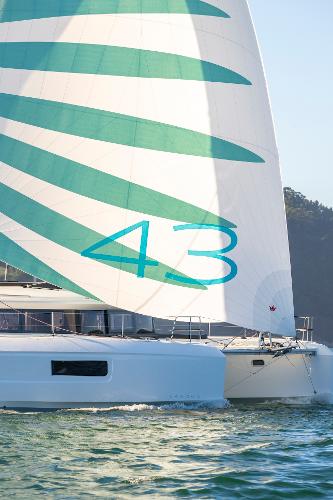 2025 Lagoon 43 catamaran sailing with green and white sail on open water.
