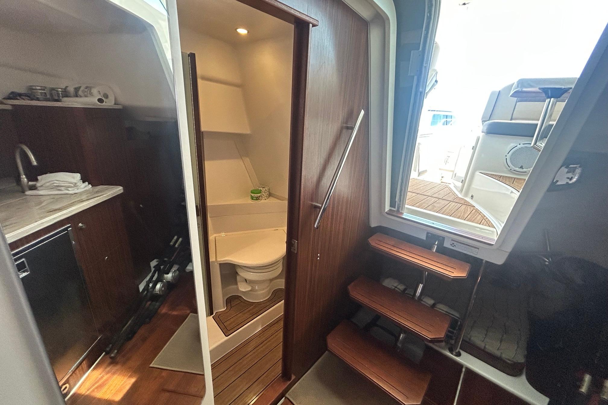 Interior of 2019 Pursuit OS 355 Offshore boat with wooden cabinetry and compact bathroom.