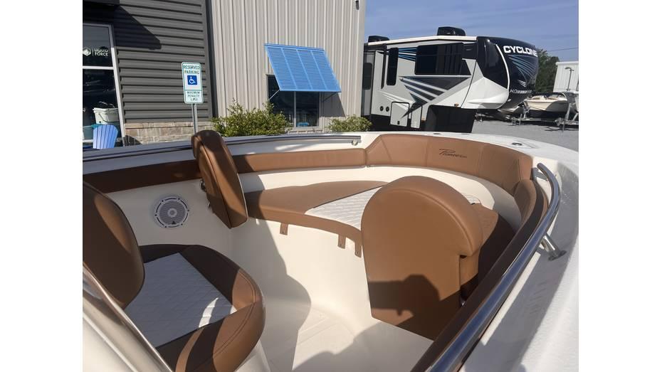 2025 Pioneer 202 Islander boat interior with brown seating, parked near RVs and a building.