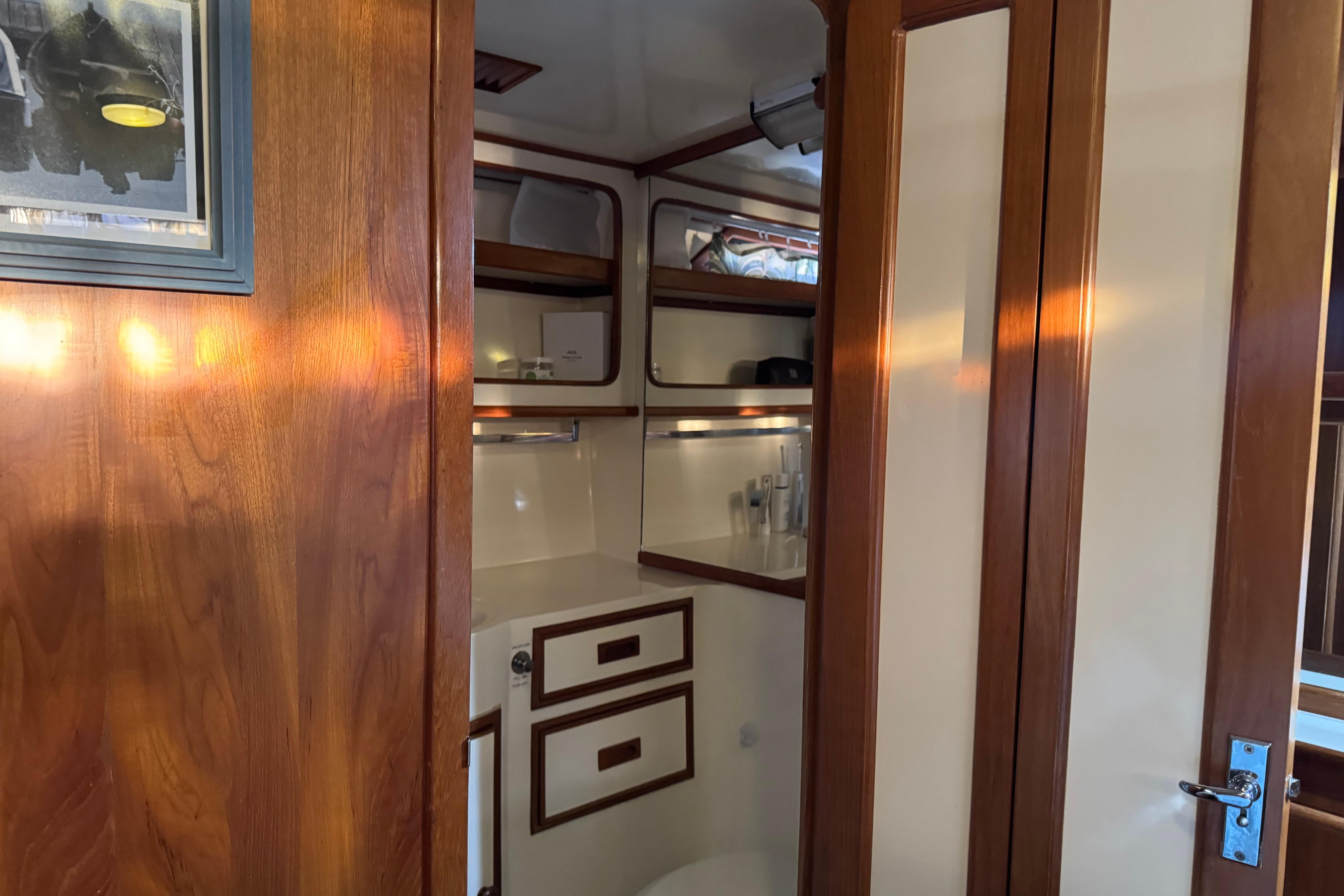 Wood-paneled bathroom interior of a 1987 President 37 yacht, featuring storage cabinets and a mirror.