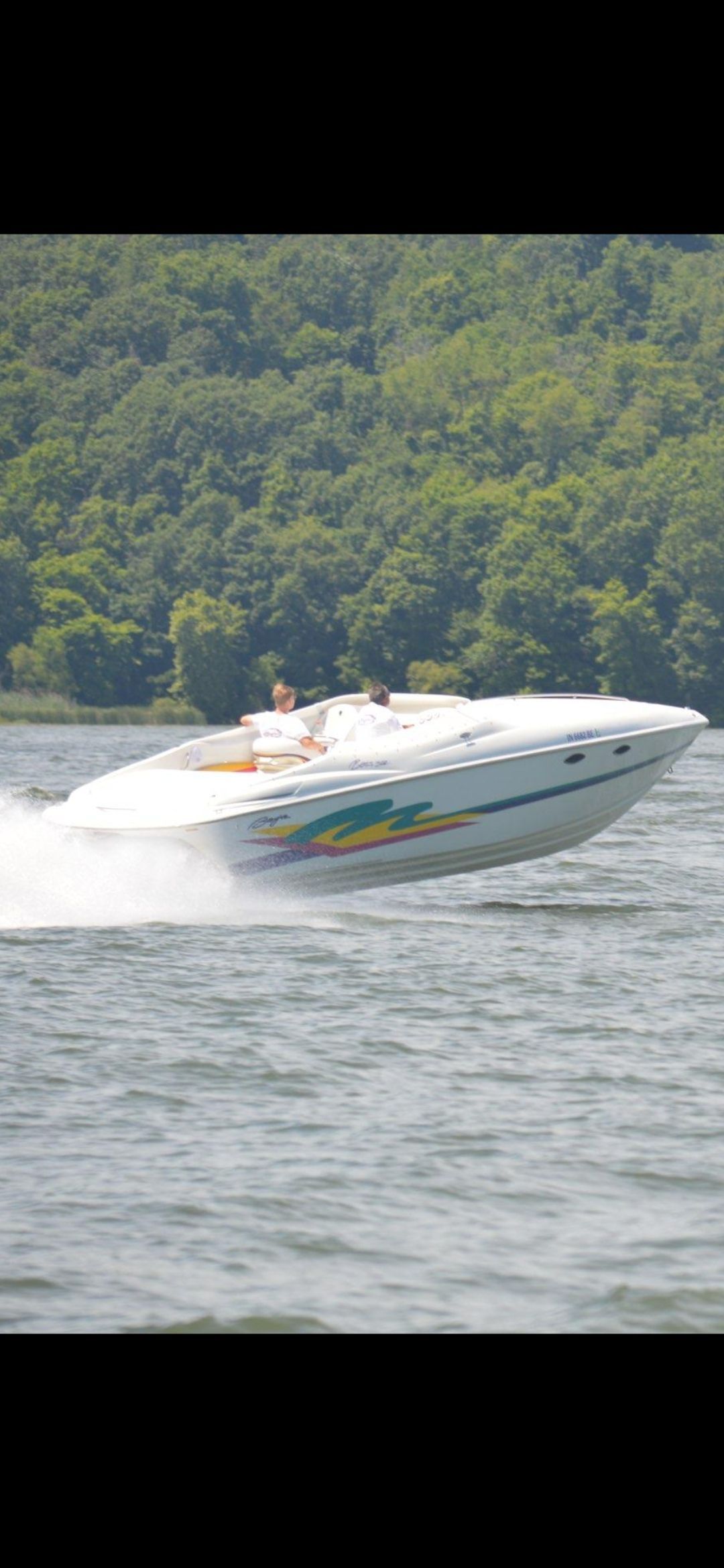 A 1996 Baja 302 Boss speeding across the water, surrounded by green trees.