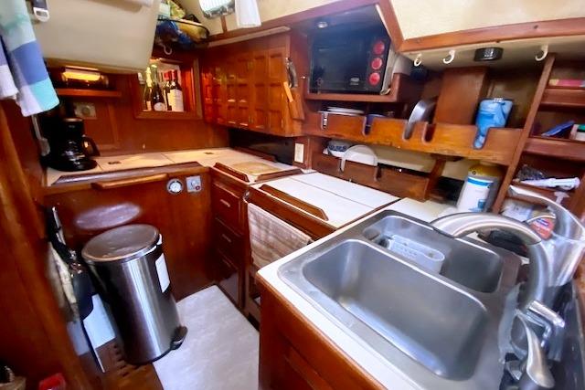 Compact kitchen in a 1982 Endeavour 40 sailboat, featuring wooden cabinetry and modern appliances.