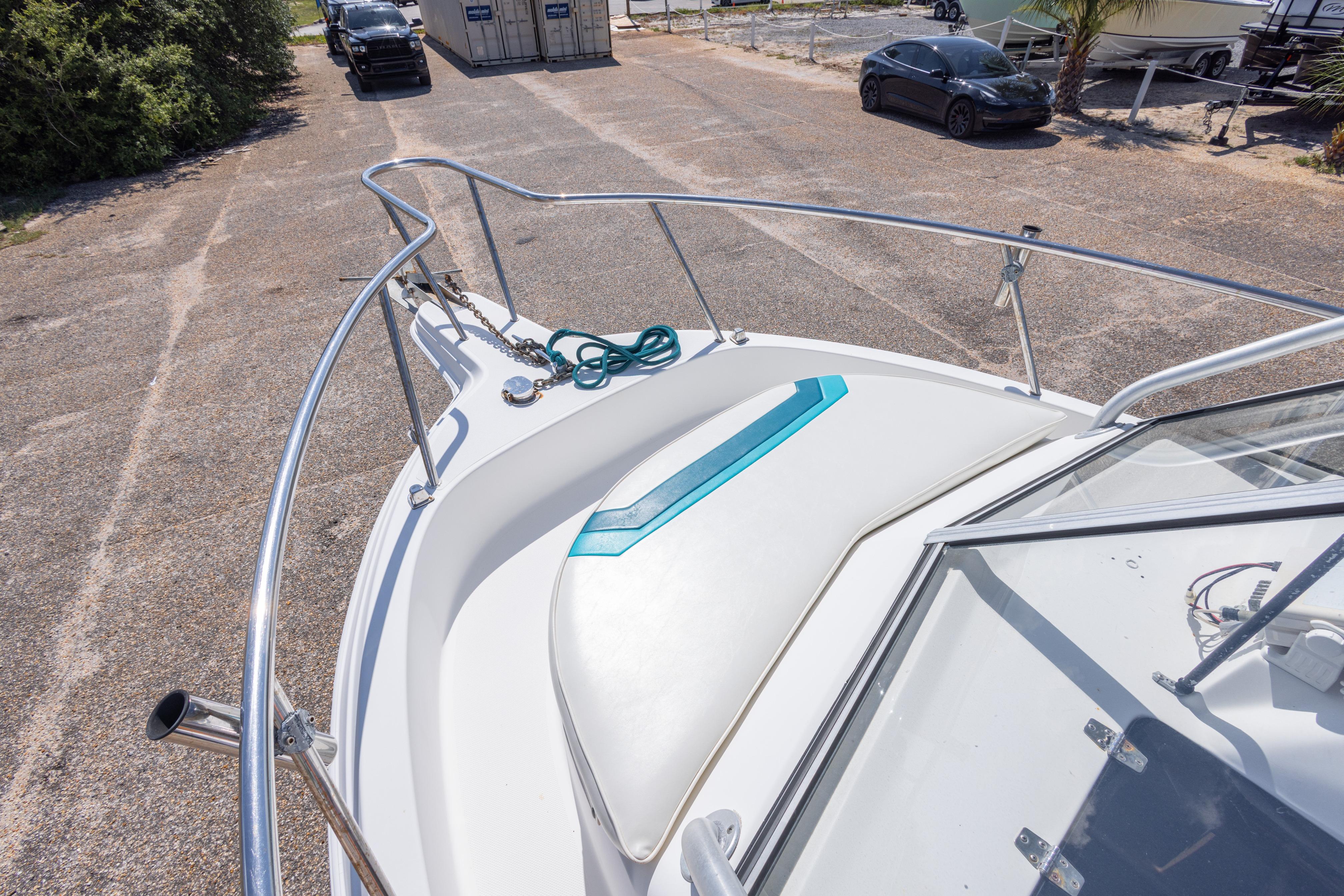 1999 Aquasport 225 Explorer boat deck with railing and anchor, parked on a lot.