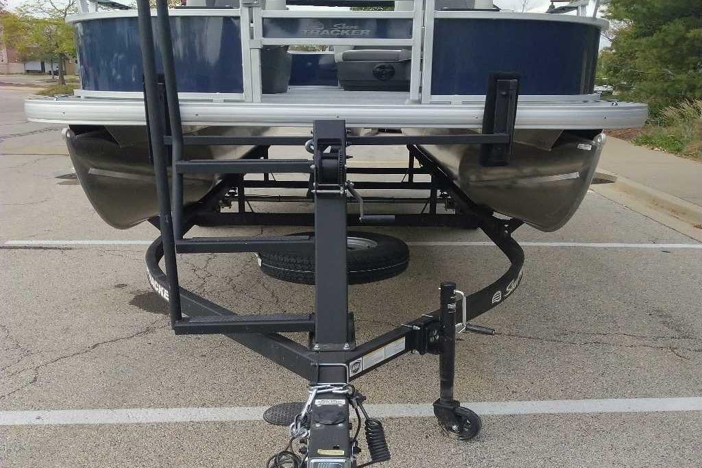 2026 Sun Tracker Bass Buggy 16 XL Select pontoon boat on trailer in parking lot.