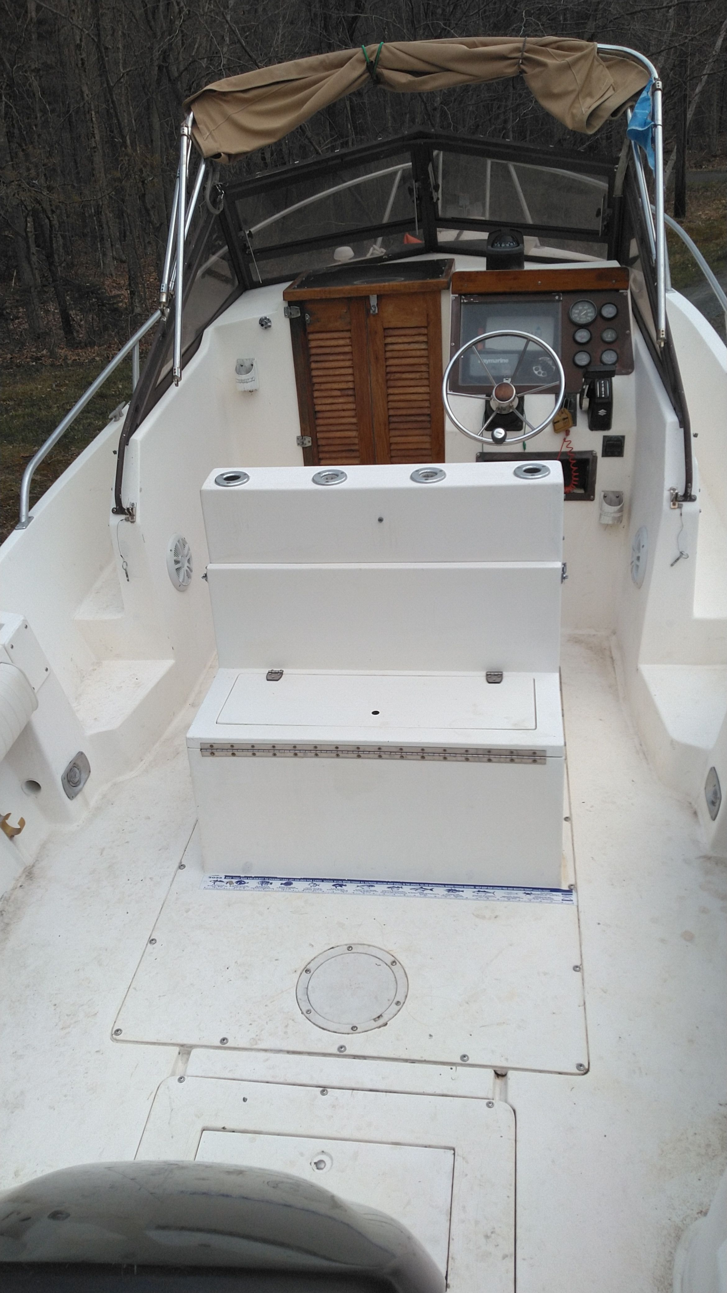 A Mako 240 walk around boat with a helm and seating, surrounded by trees.