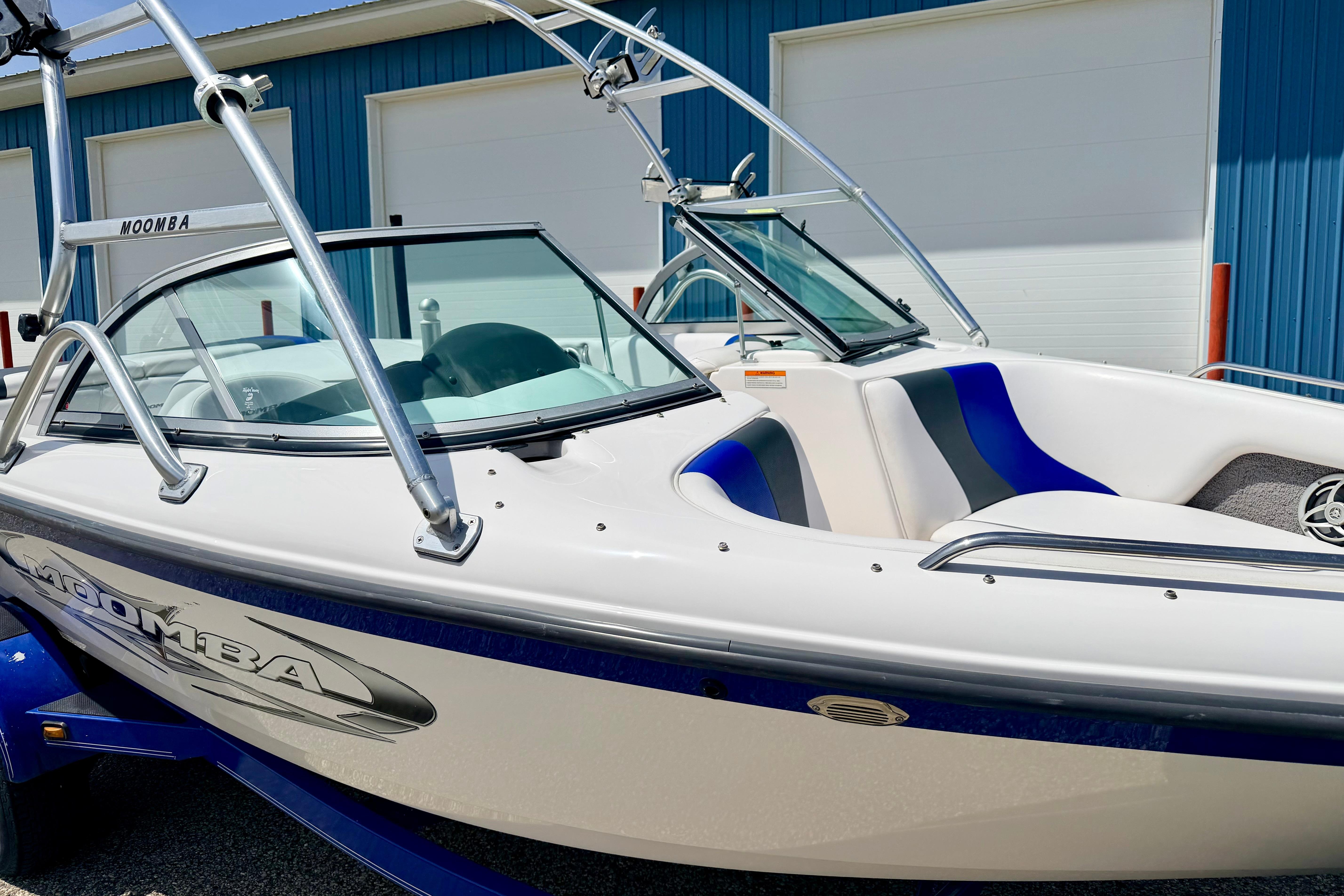 2008 Moomba Outback V boat with blue and white design, parked near a blue building.