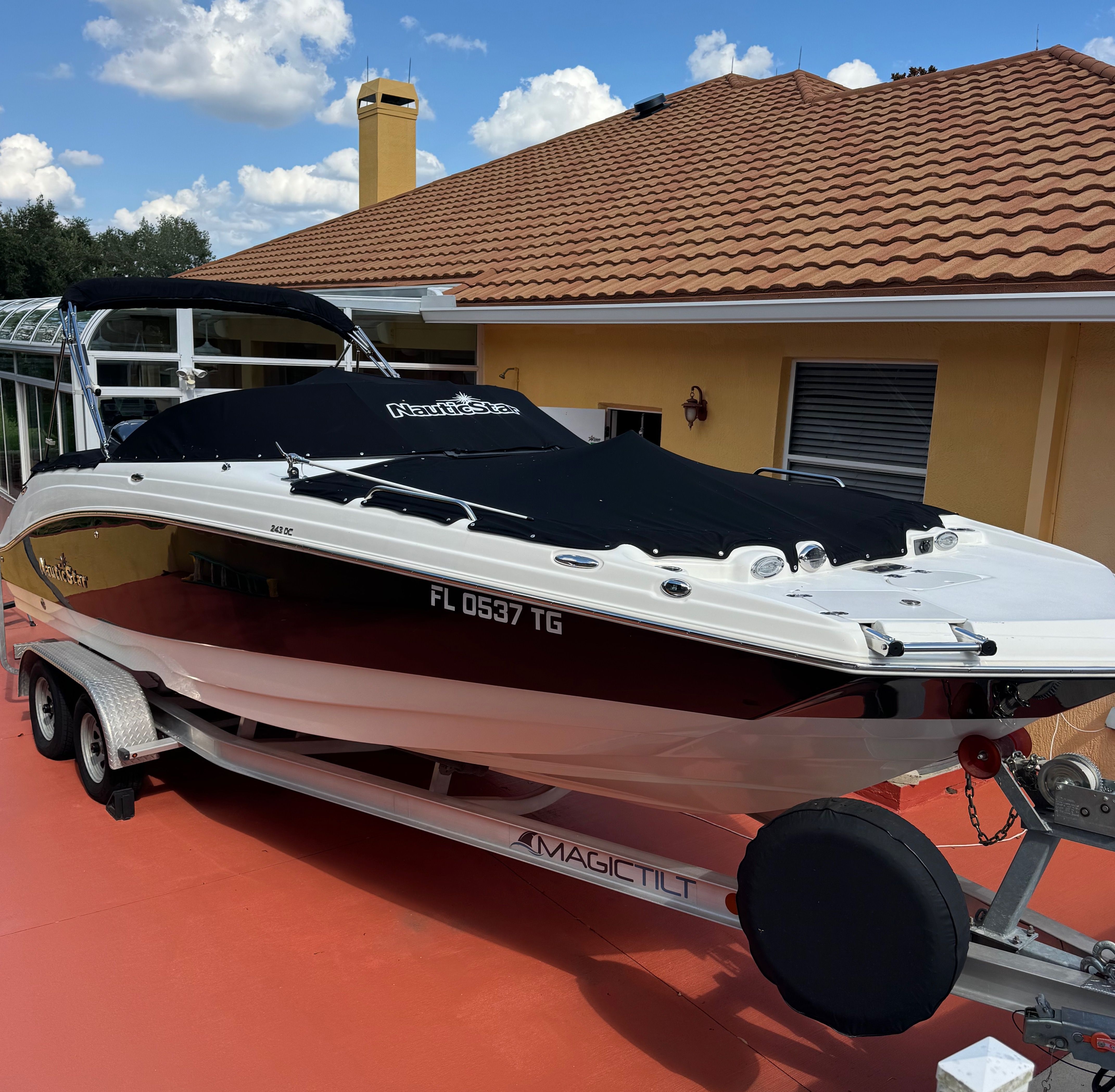 A 2022 NauticStar 243 DC boat on a trailer, parked in front of a house with a tiled roof.