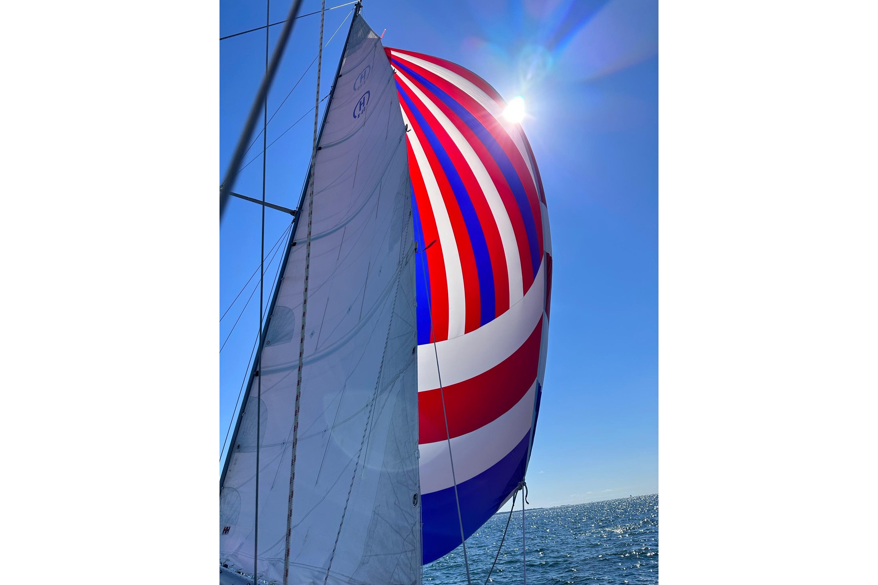Sailing yacht Hinckley Bermuda 40 with colorful spinnaker against clear blue sky.