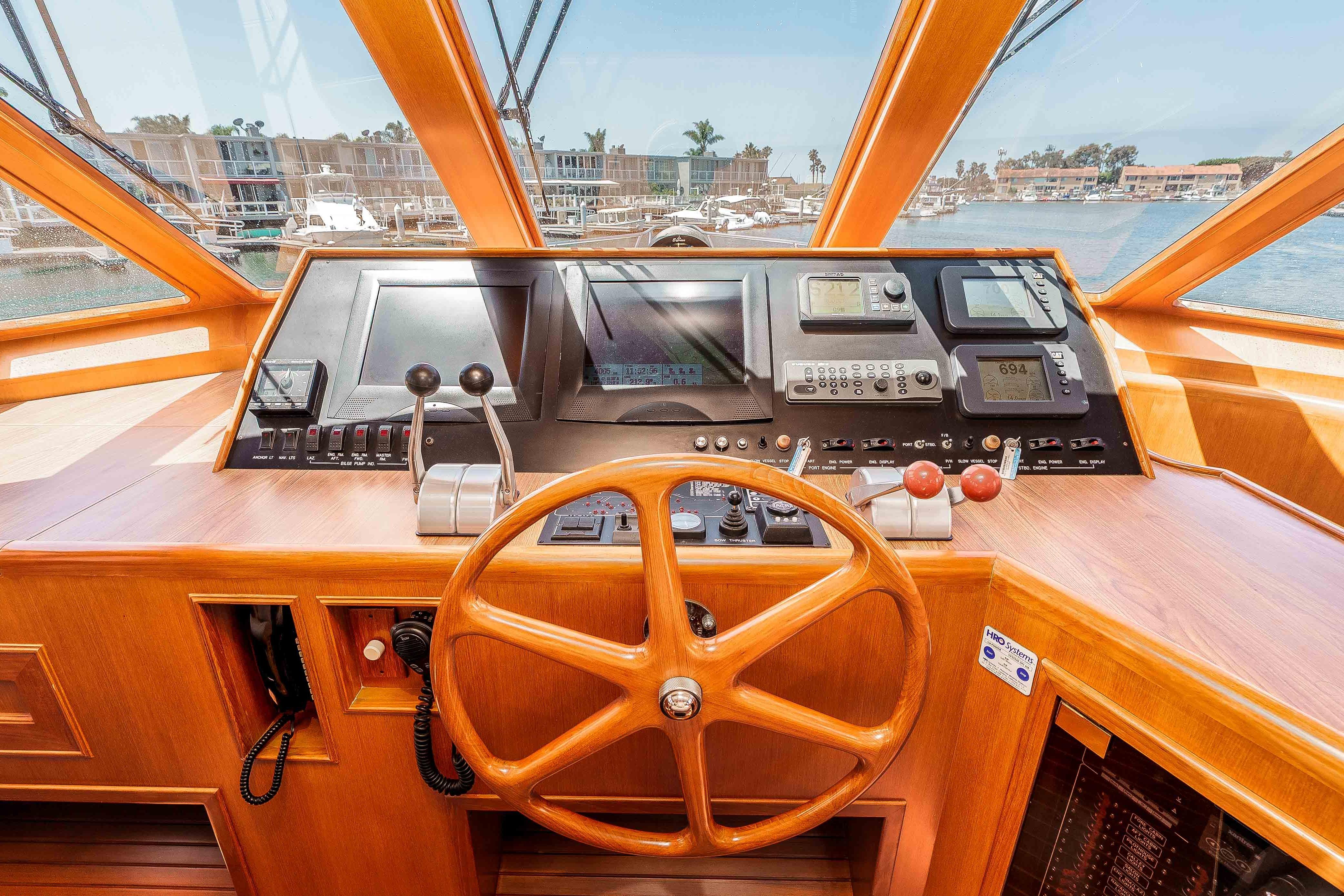 Pilothouse interior of 2005 Offshore Yachts 54, featuring wooden steering wheel and navigation controls.