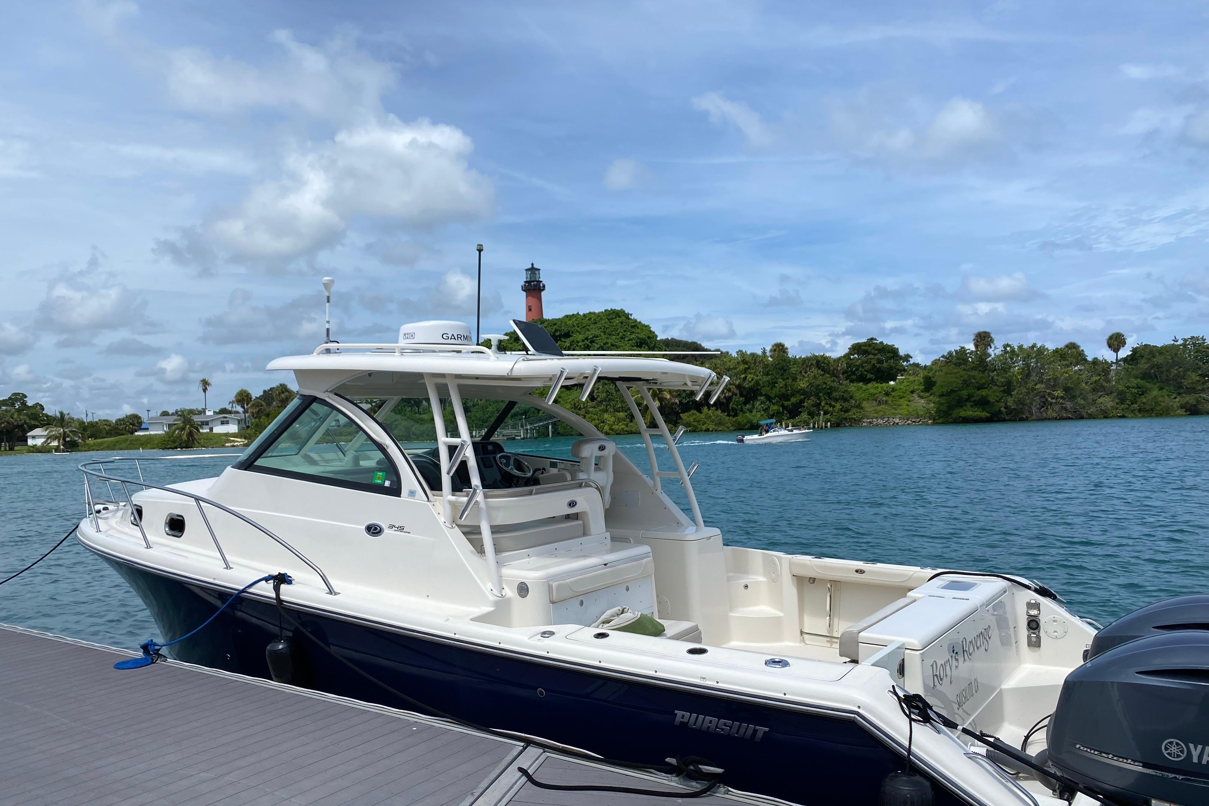 2014 Pursuit OS 345 Offshore boat docked by a scenic waterway with lush greenery.