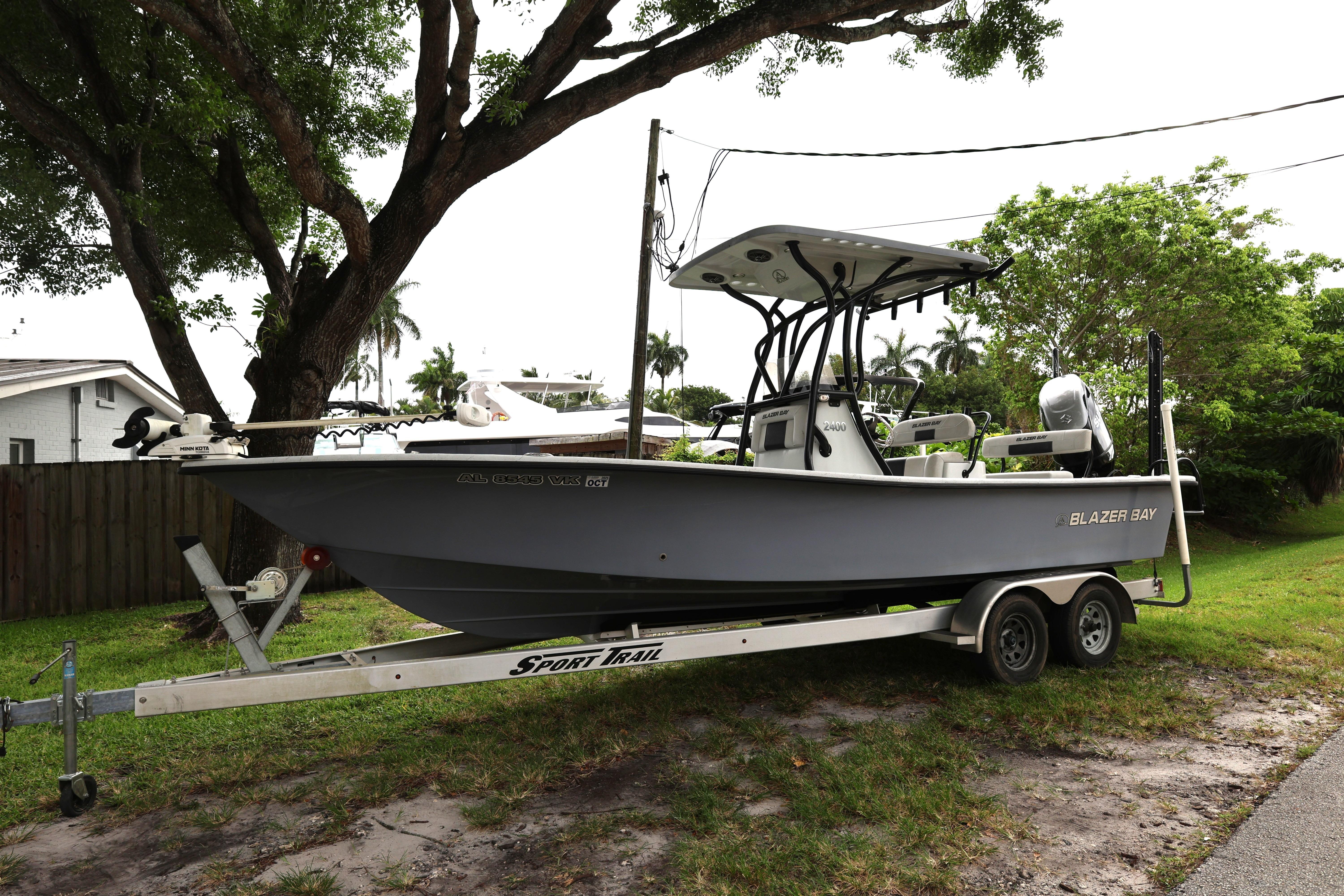 2021 Blazer Bay 2400 boat on trailer, parked outdoors under trees.