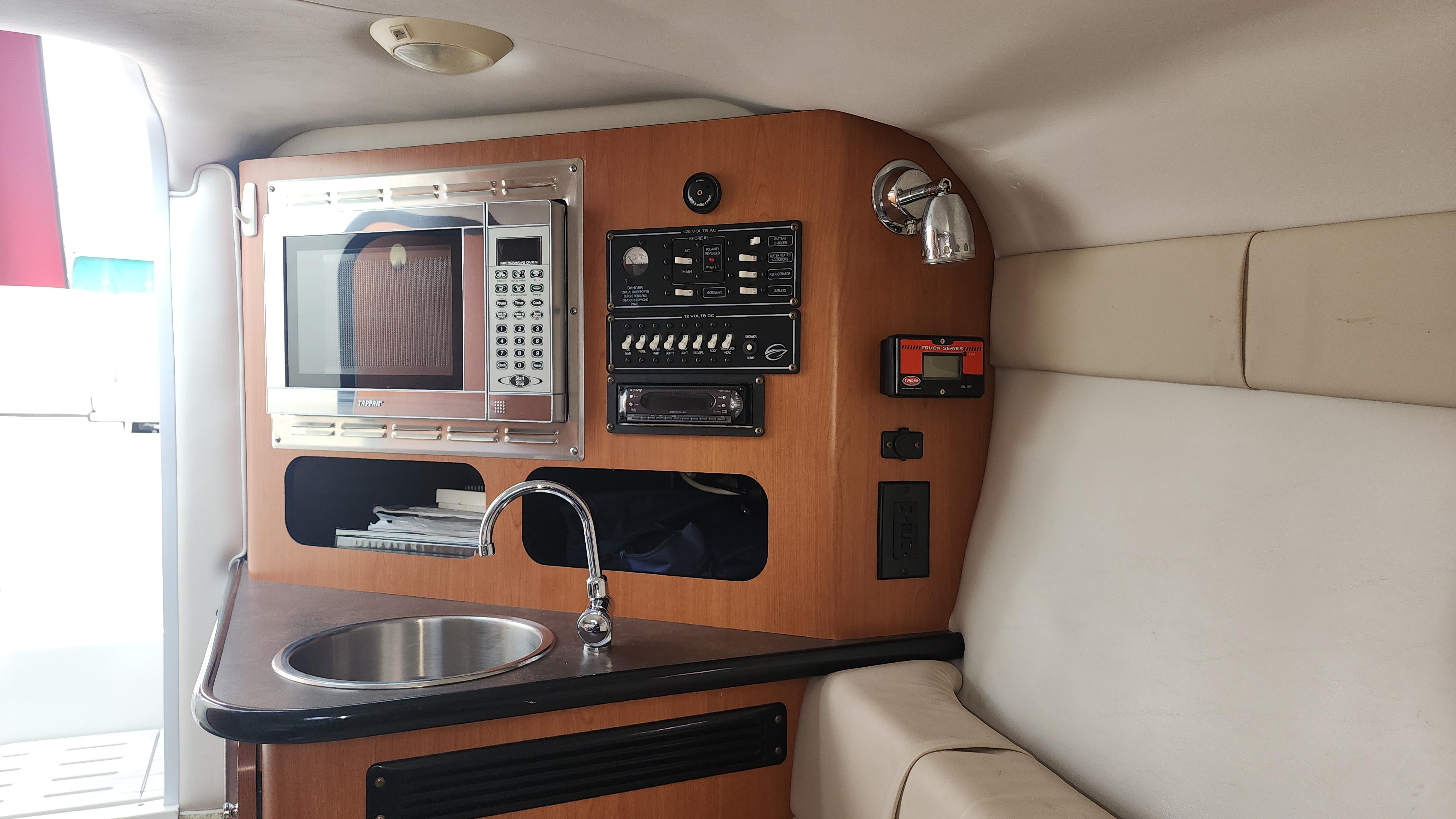 2008 Crownline 255 CCR boat interior with kitchenette, featuring a microwave, sink, and control panel.