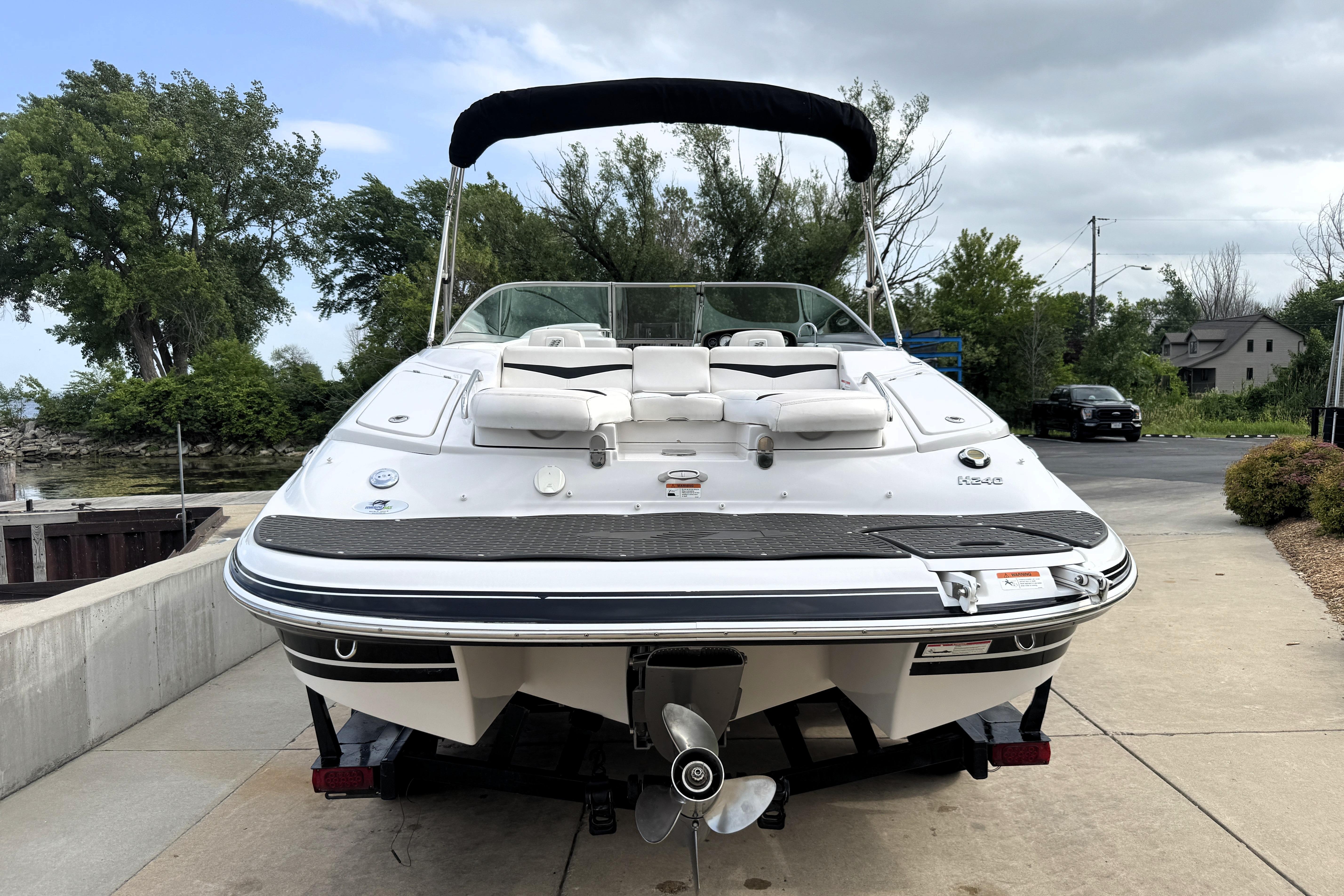 2008 Four Winns H240 boat with white seating, docked on a concrete ramp, surrounded by trees.