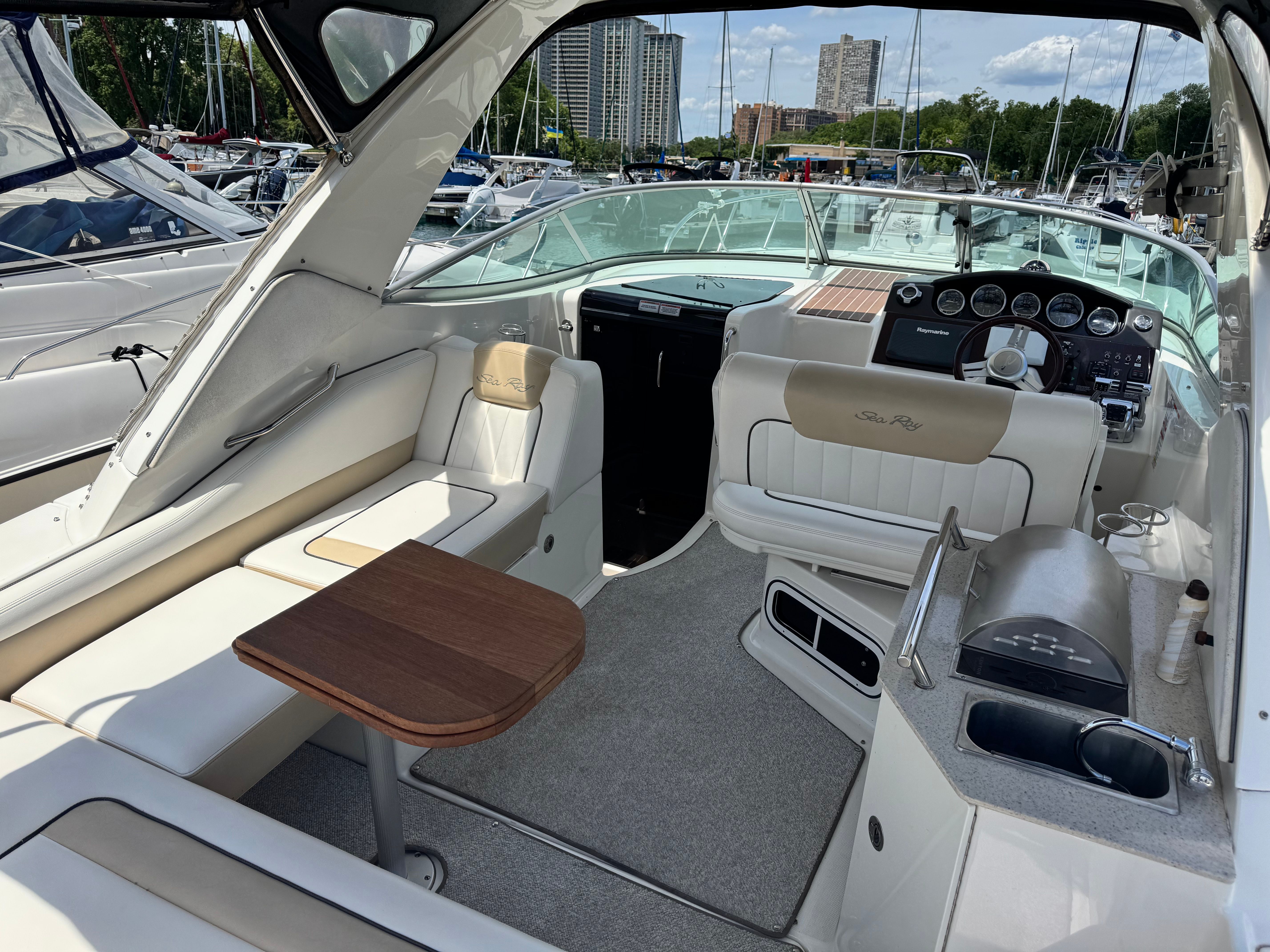 The image shows the cockpit of a Sea Ray Sundancer 310 with beige seating and a wooden table.