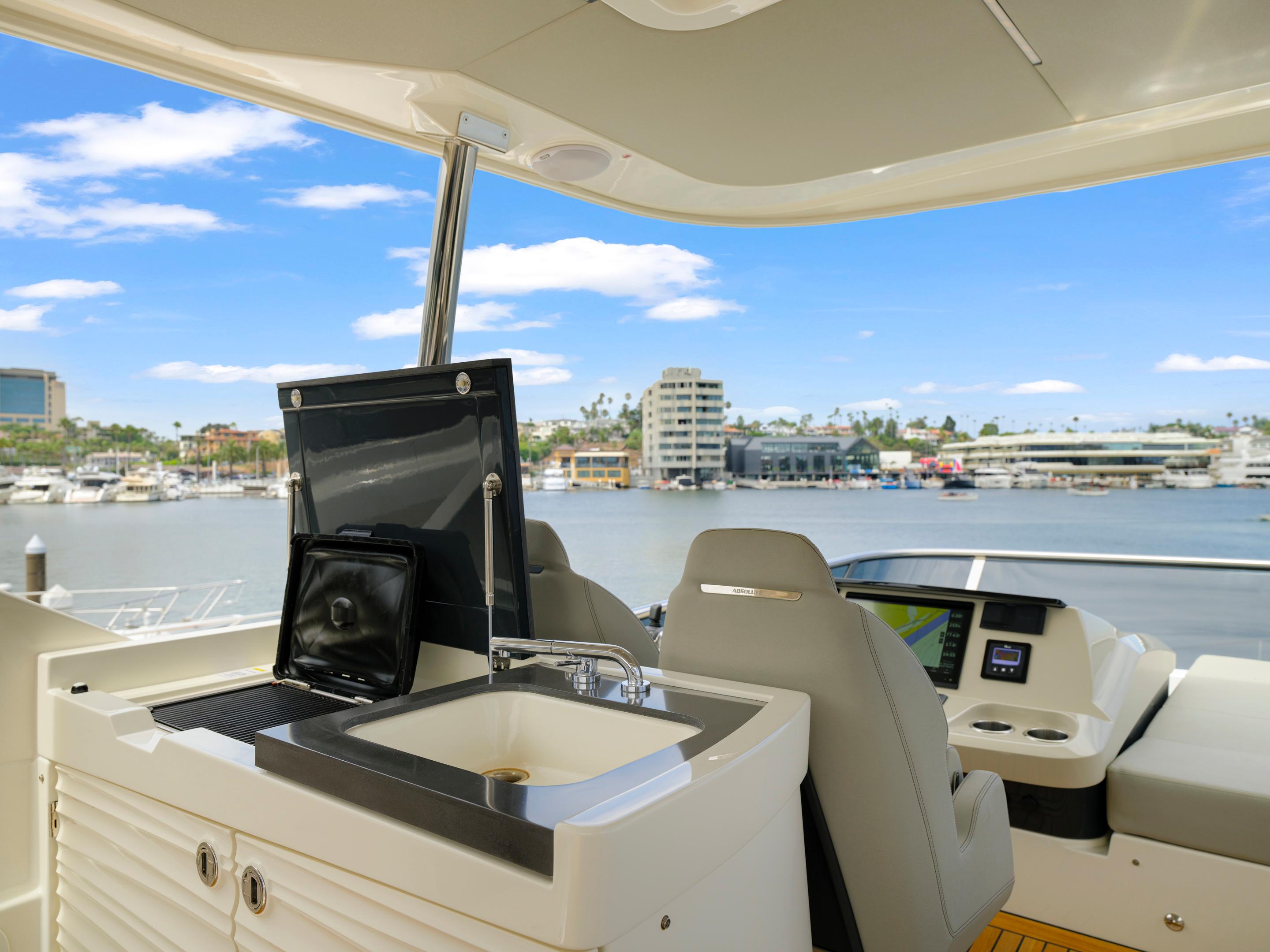 Flybridge of 2024 Absolute 60 Fly yacht with sink and seating, overlooking marina.