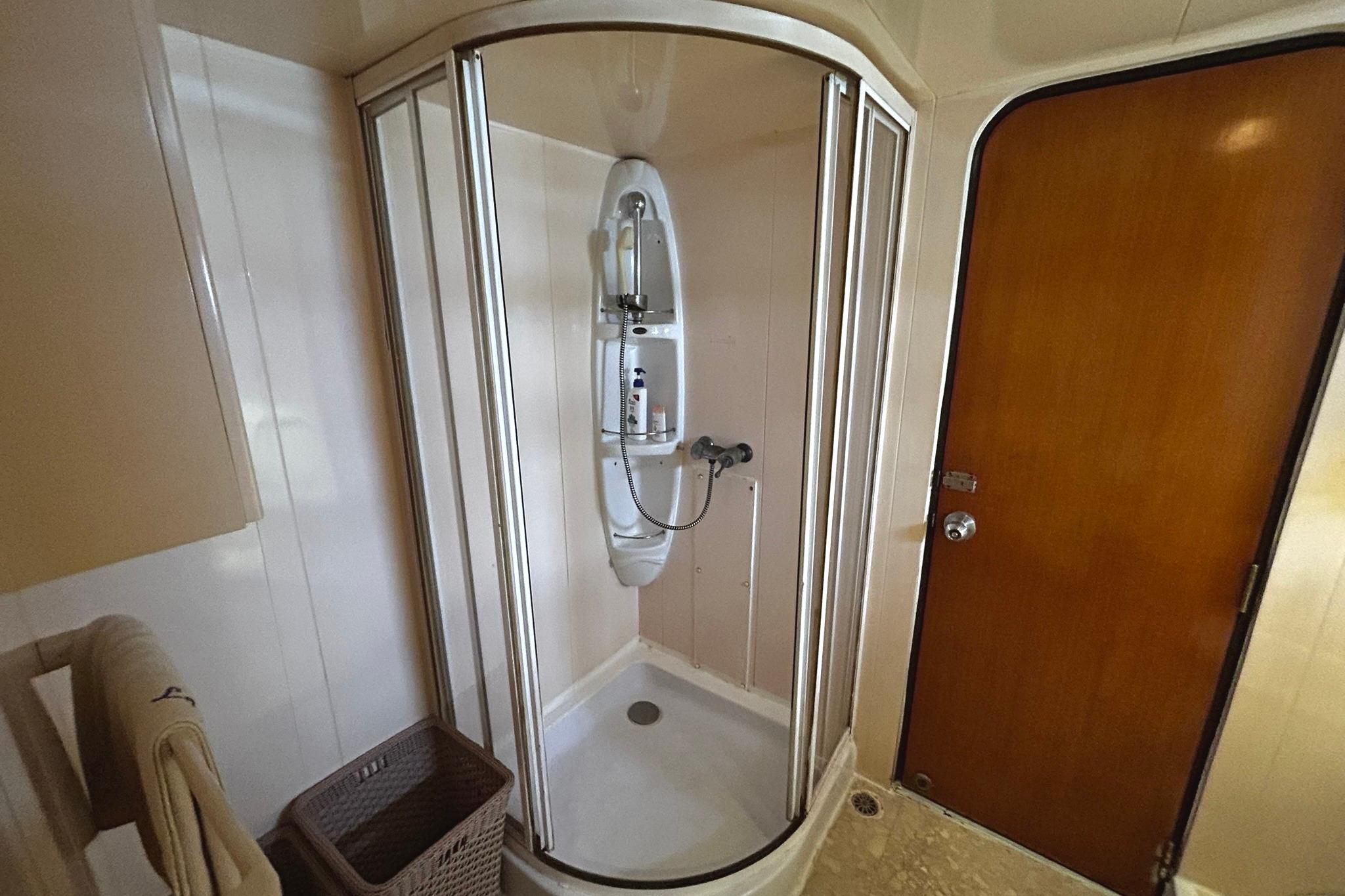 Compact shower cabin in a 1999 Custom 28M yacht bathroom with wooden door and towel rack.