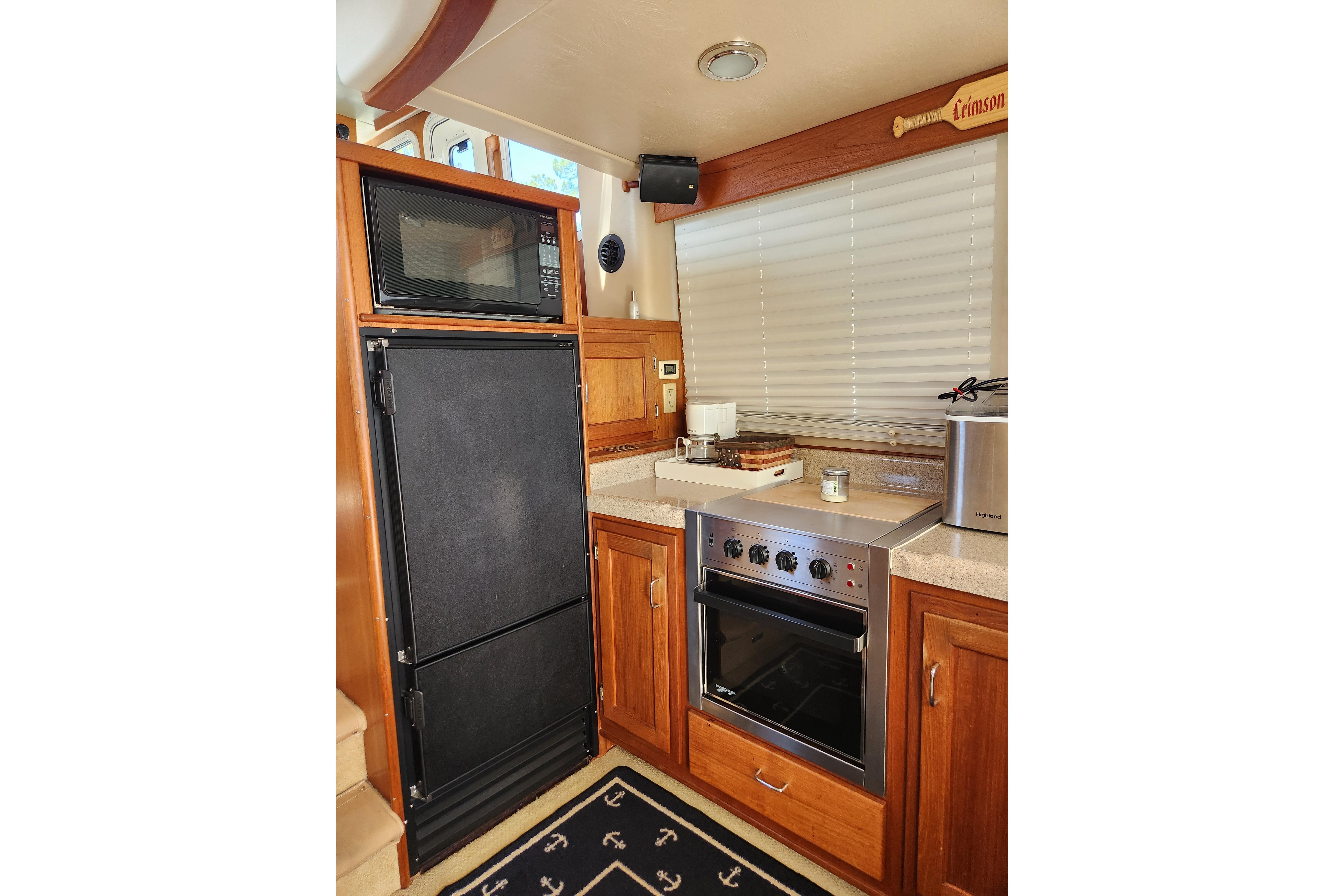 Compact kitchen in a 2006 American Tug AT boat with stove, microwave, and wooden cabinetry.