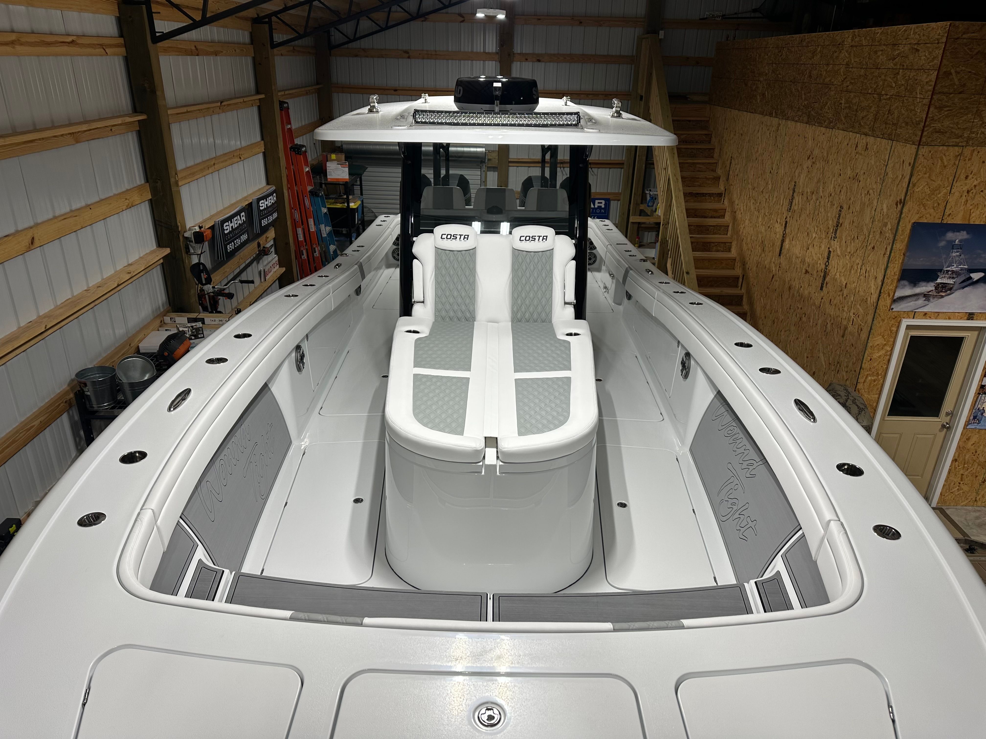 The image shows a modern boat with a spacious deck and white seating inside a warehouse.