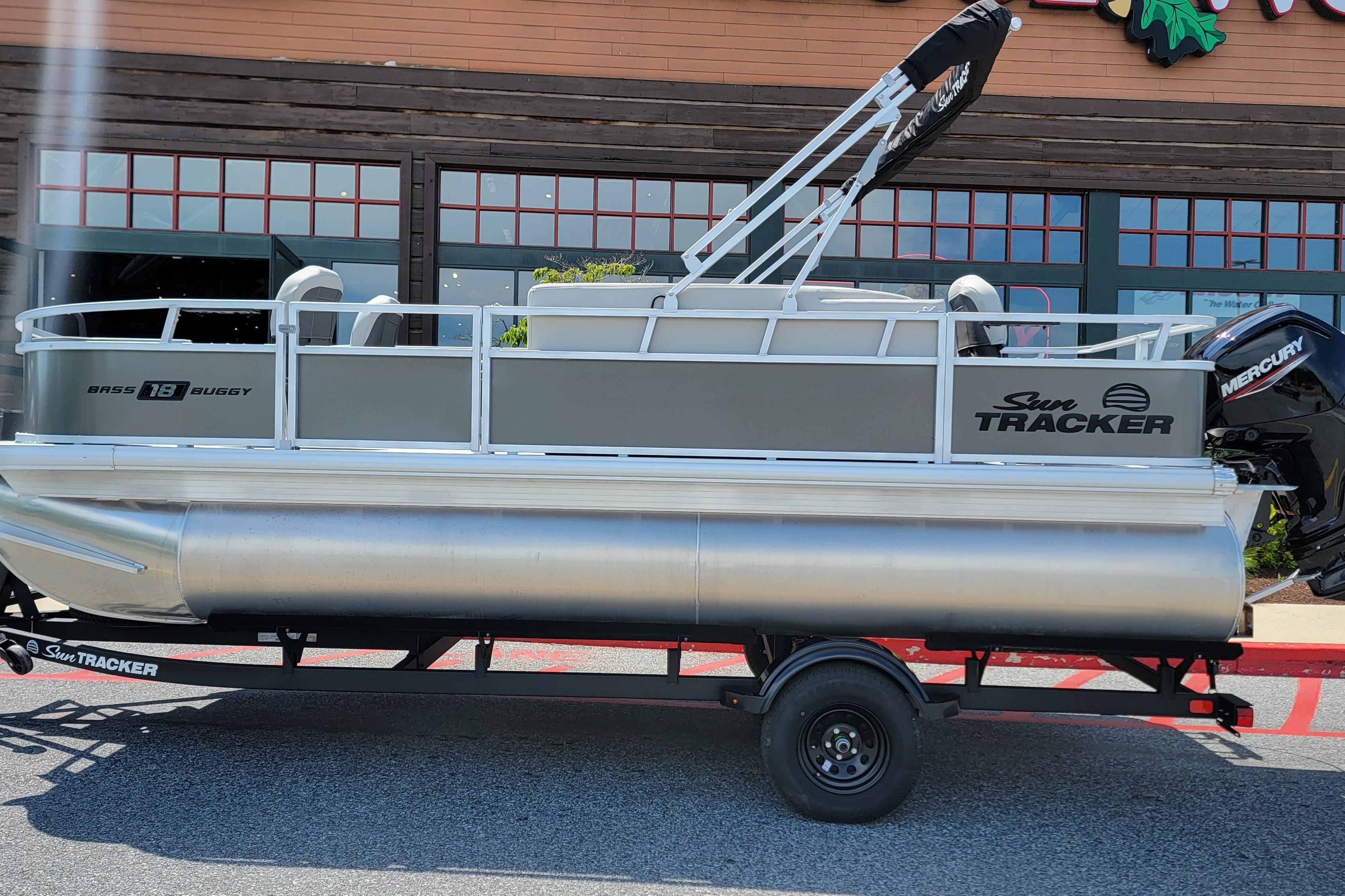 2026 Sun Tracker Bass Buggy 18 DLX pontoon boat on trailer, parked outside a building.