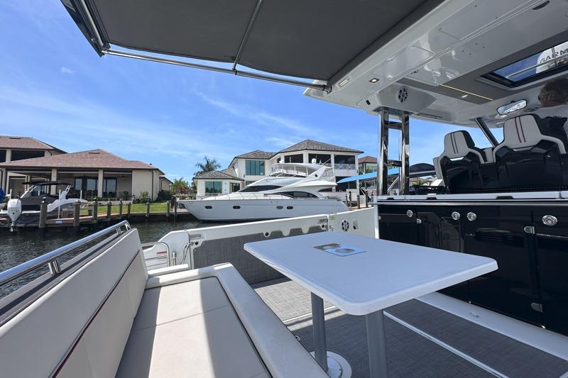 2022 Jeanneau Leader 12.5 WA boat interior with seating and table, docked near waterfront homes.