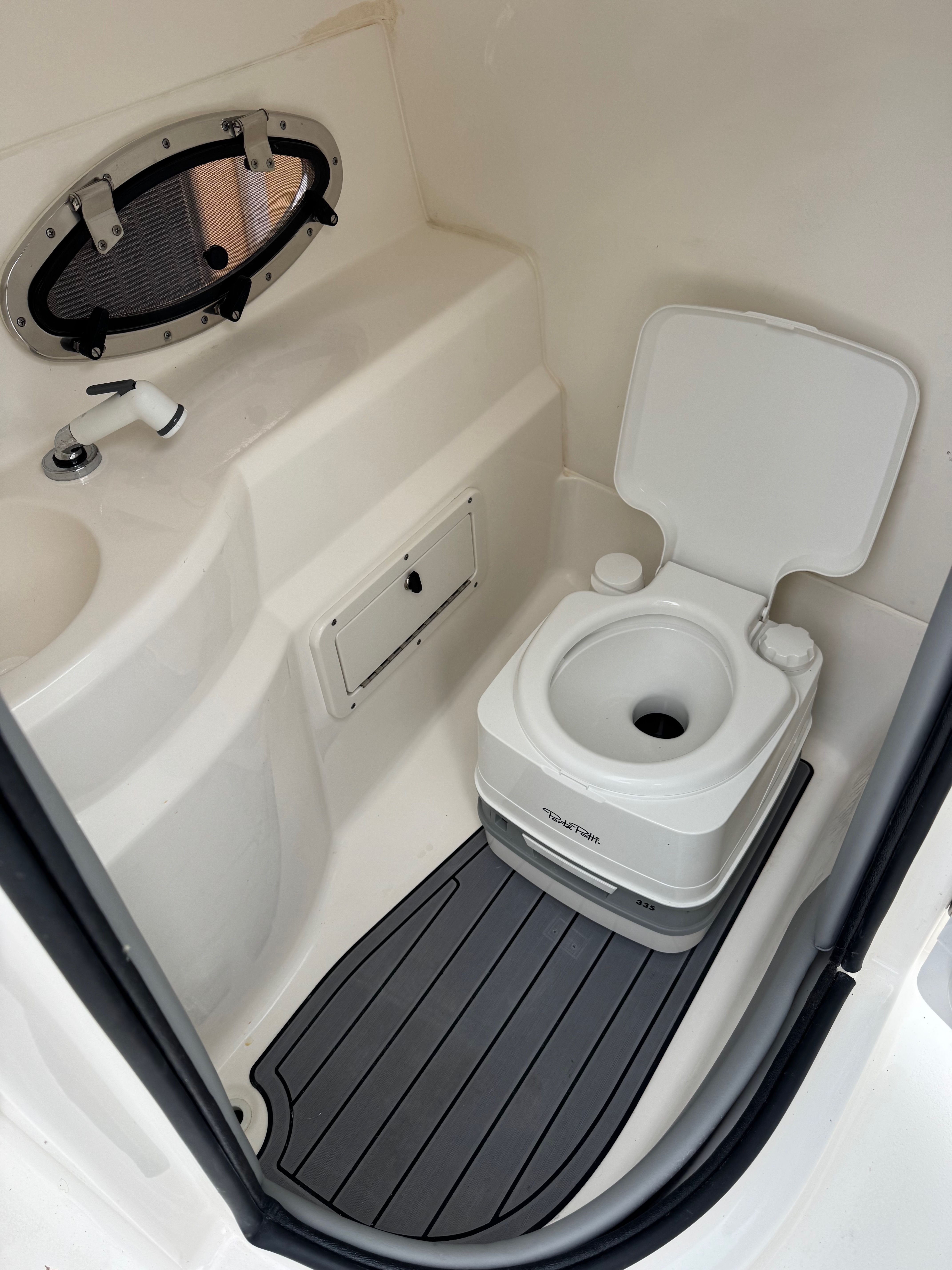 The image shows a compact boat toilet with a small sink and a porthole.