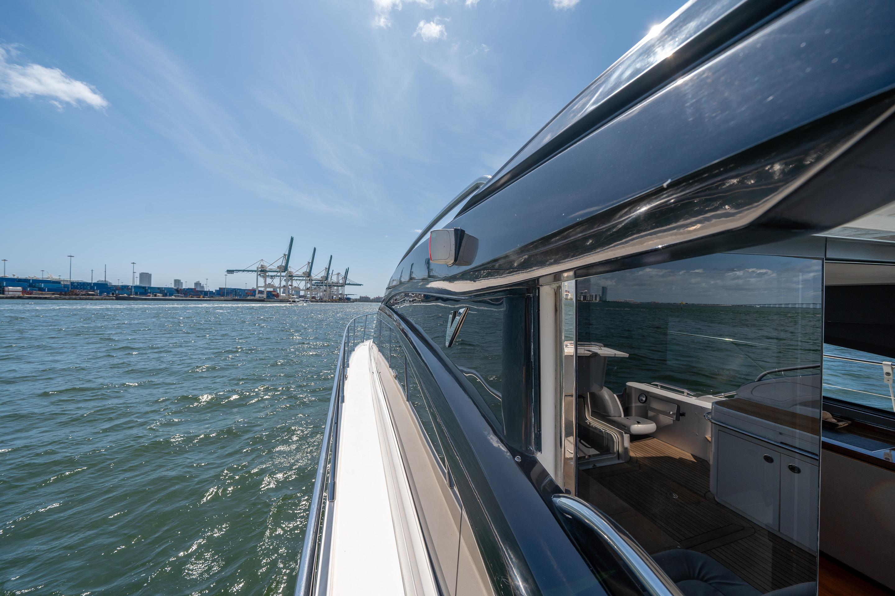 Sleek 2012 Princess V52 yacht cruising near industrial port under clear blue sky.