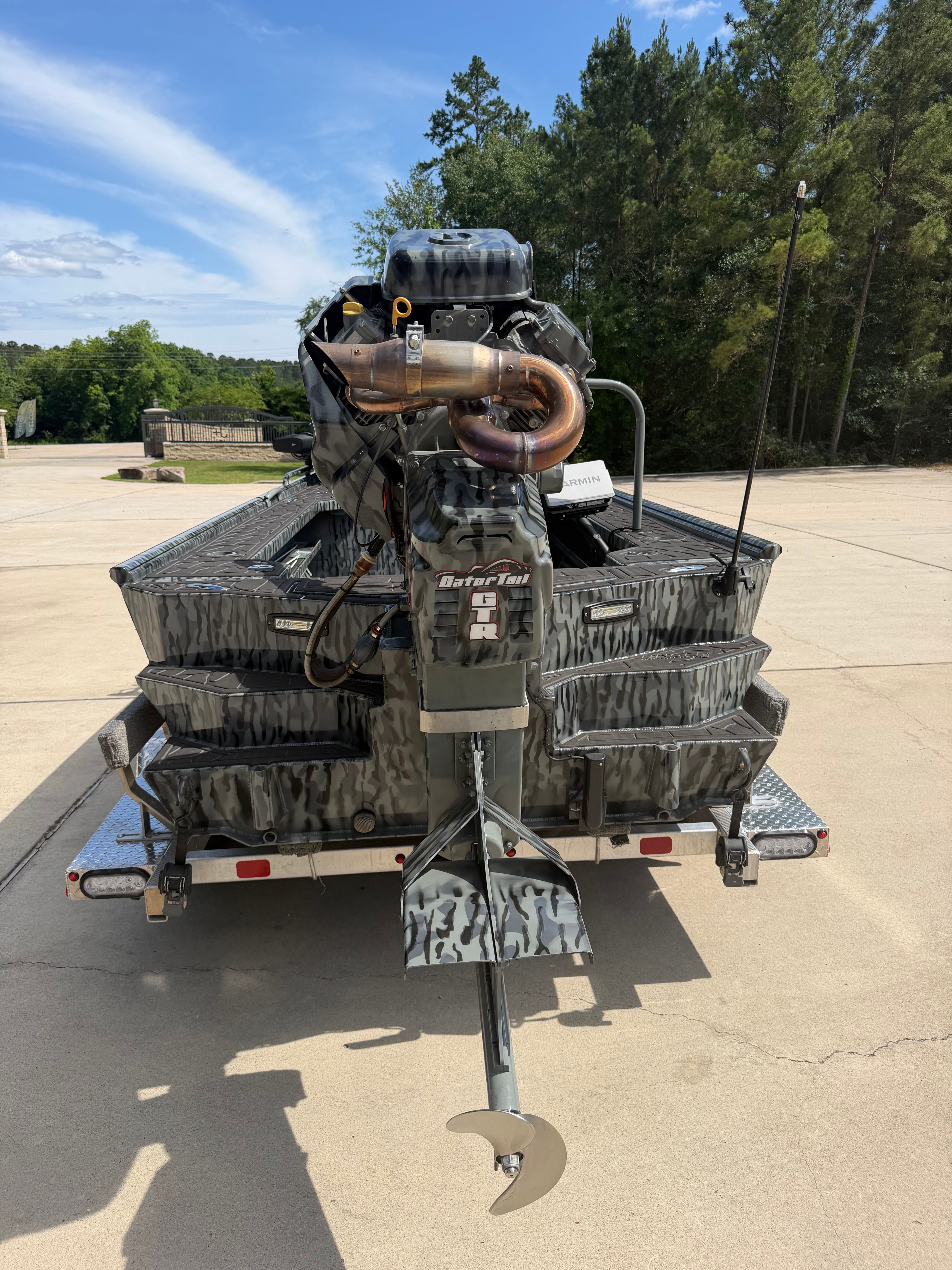 A gray boat with a large motor is on a trailer in a parking area.