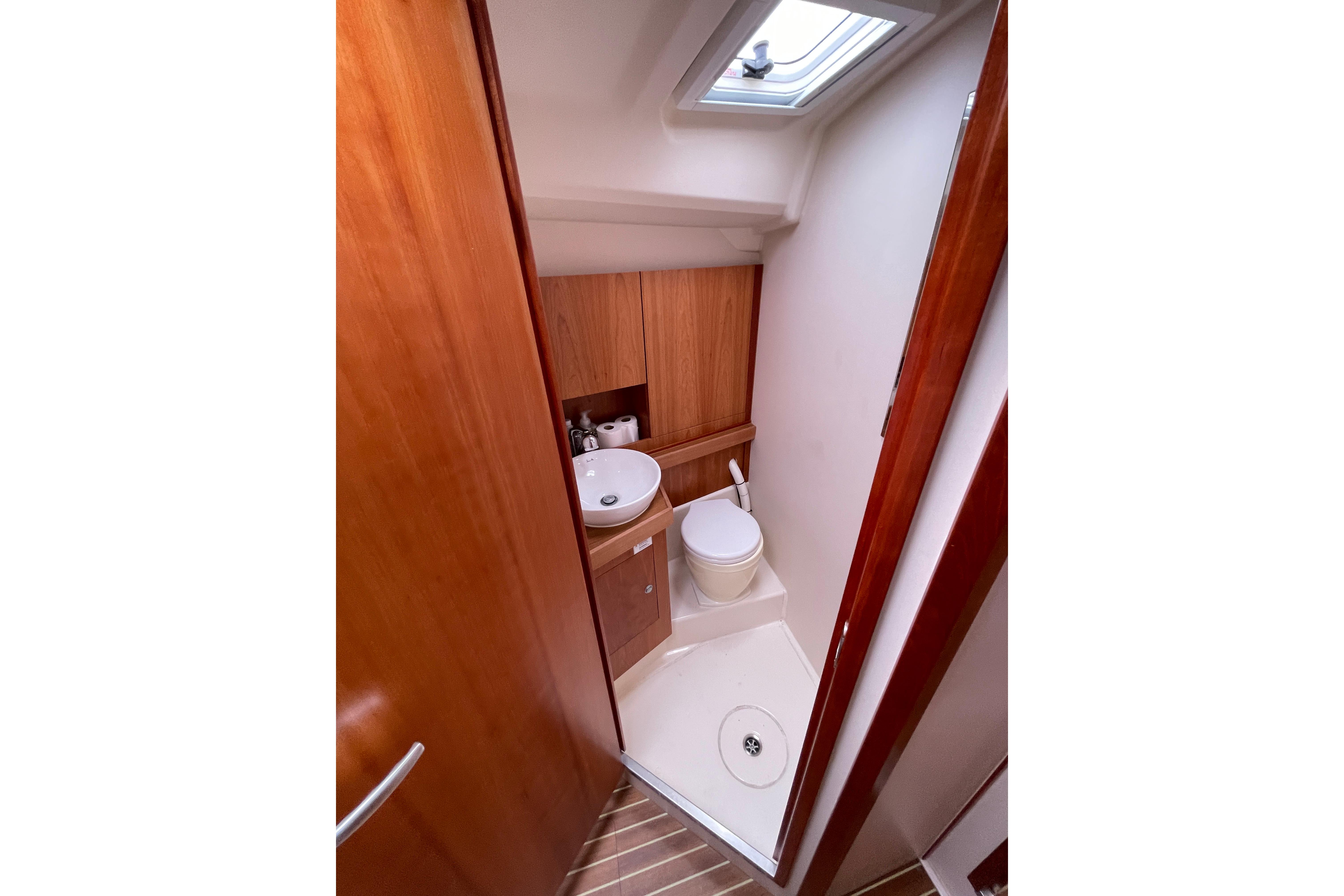 Compact bathroom in a 2014 Hanse 415 yacht, featuring wooden cabinetry and a skylight.