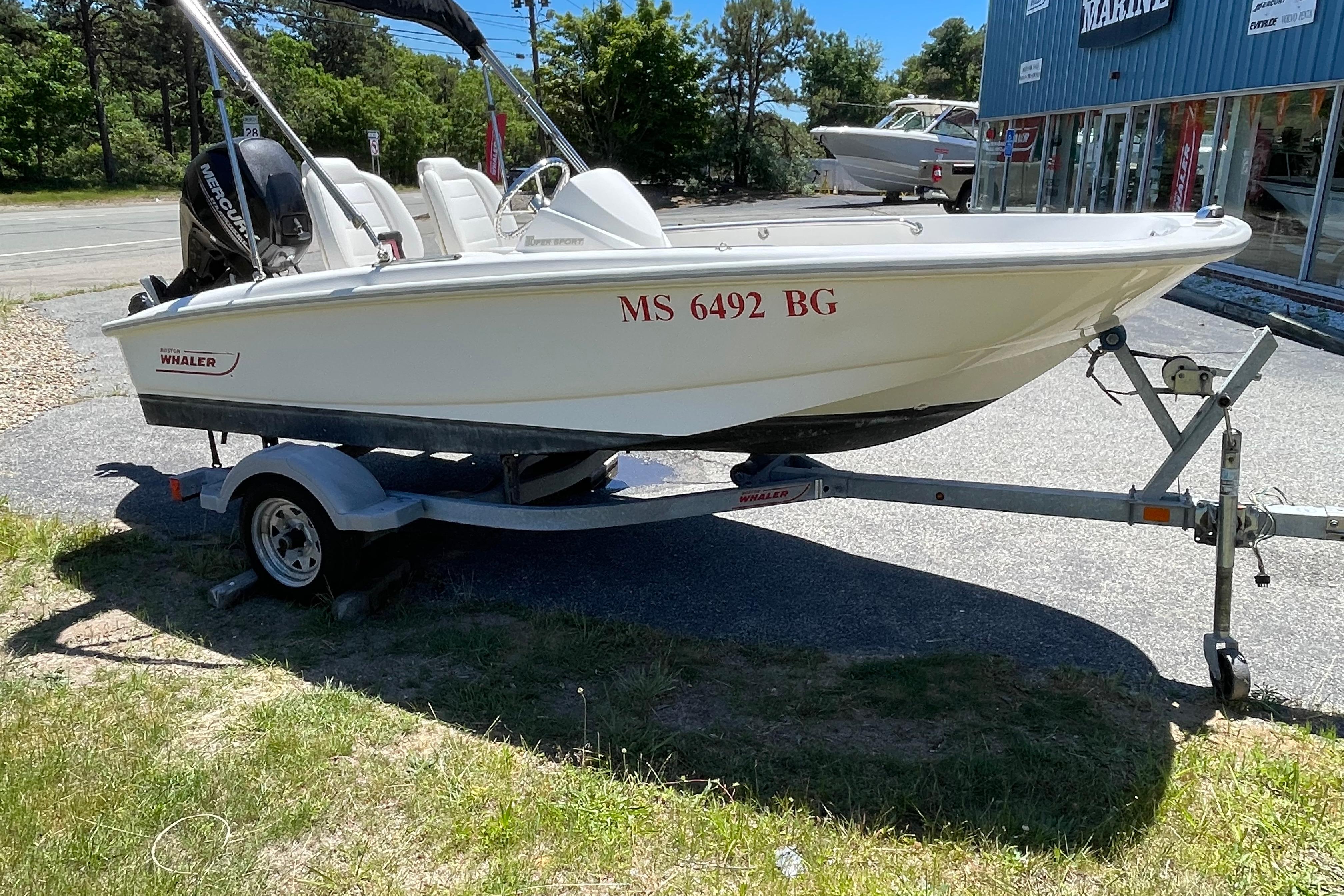 2017 Boston Whaler 130 Super Sport boat on trailer, parked outdoors near a marine shop.