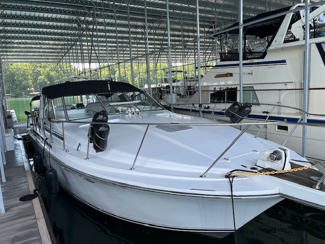 A 1989 Trojan 370 Express is docked under a covered area. The boat features a white deck.