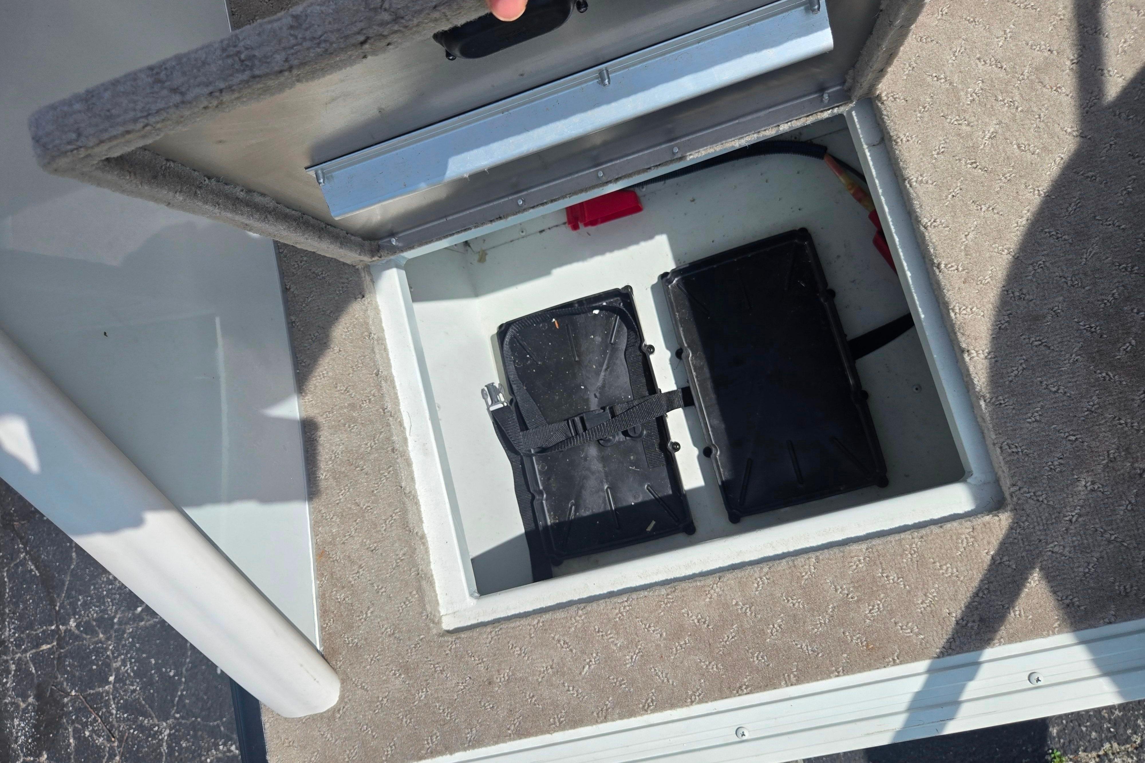 Open storage compartment on 2015 Lowe Sport Deck 224 boat, revealing battery boxes.