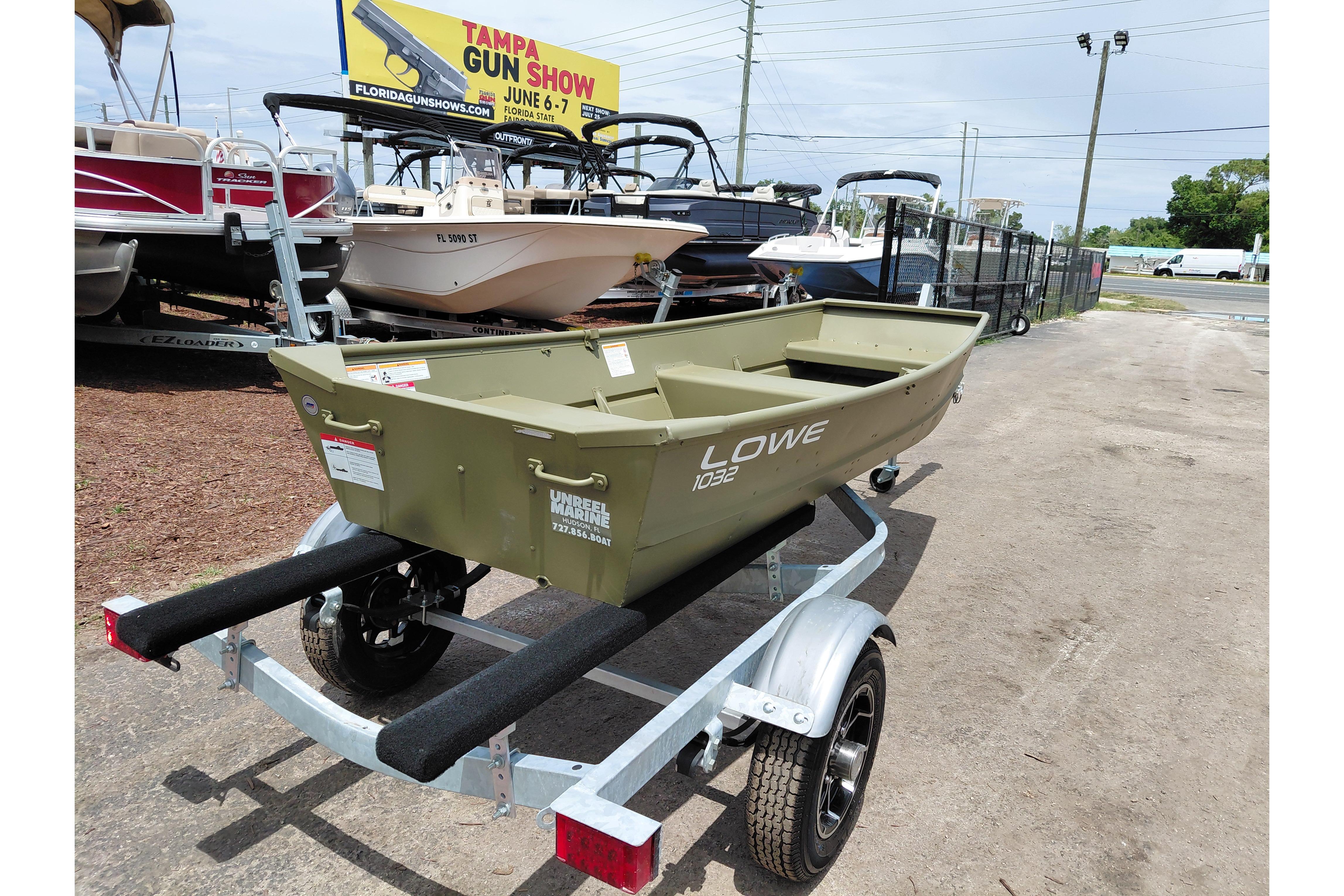 2026 Lowe L1032 Jon boat on trailer at dealership, with Tampa Gun Show billboard.