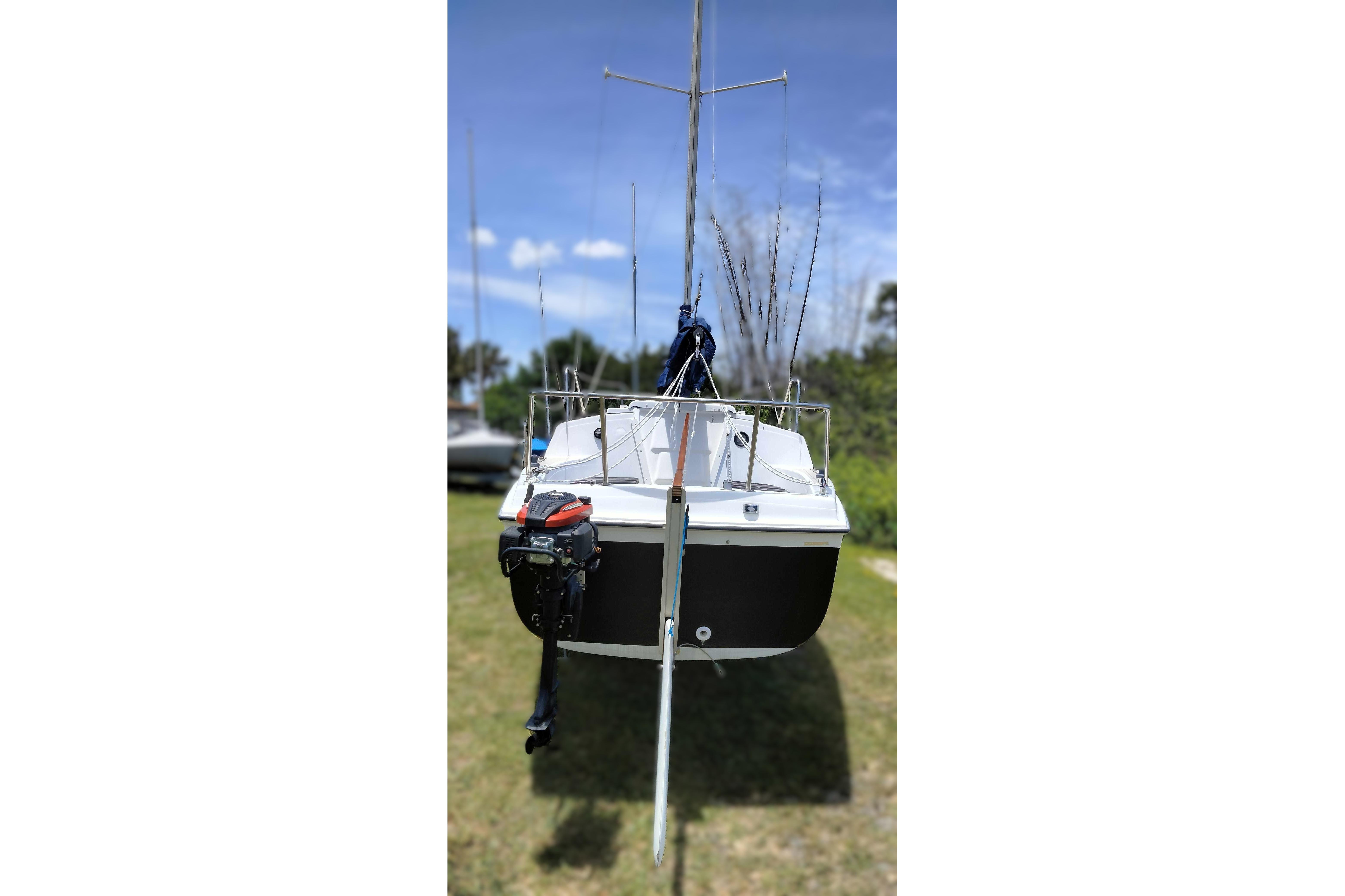 1980 MacGregor 25 sailboat with outboard motor on grassy area under blue sky.