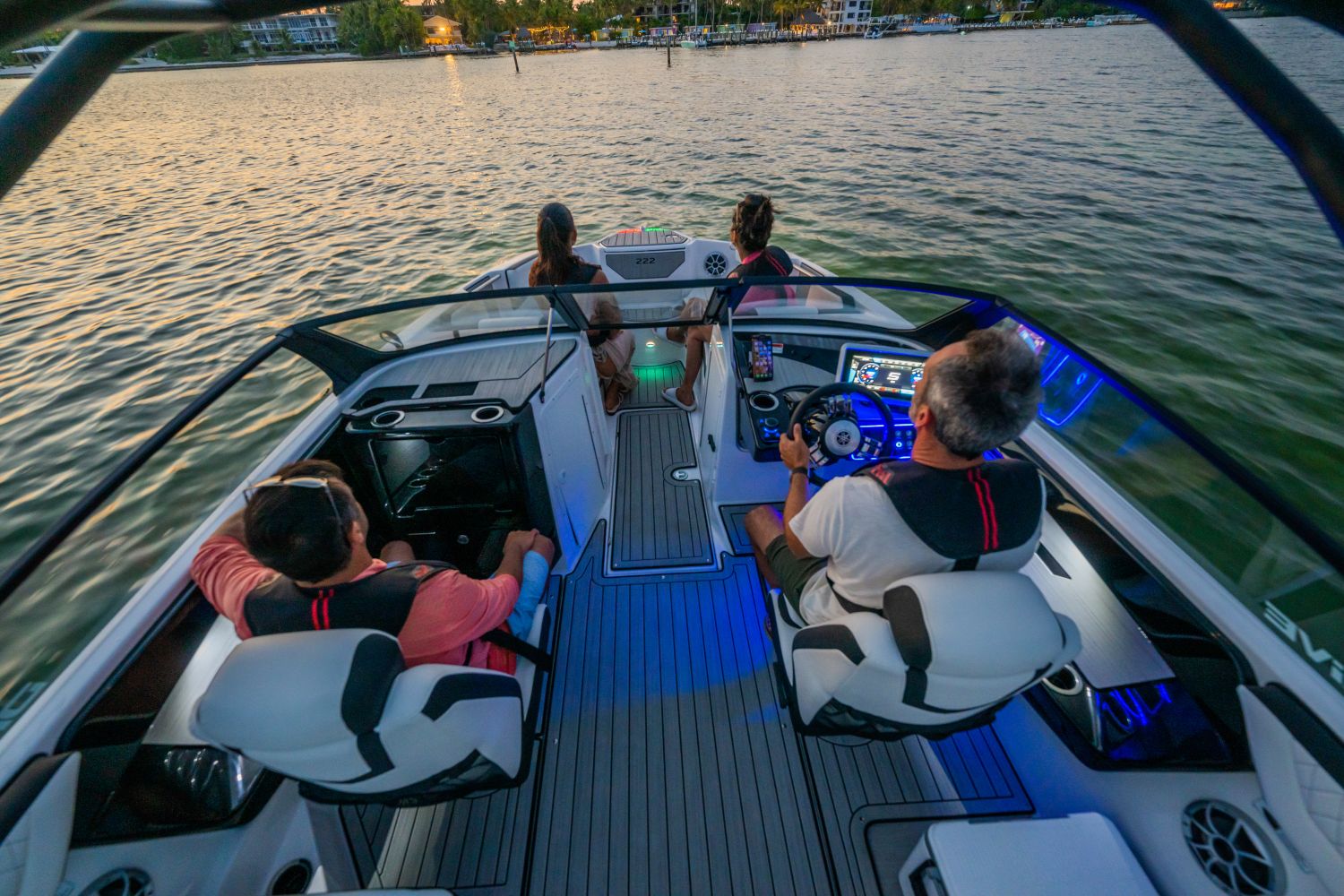Four people sit in a modern boat on a calm lake at sunset.