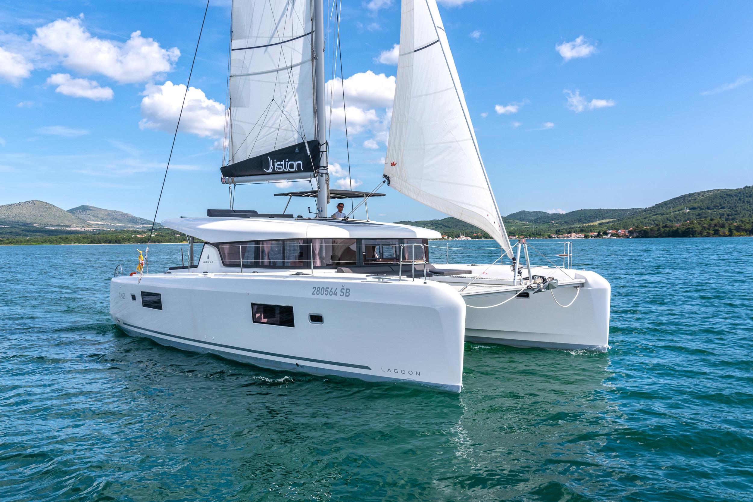 2023 Lagoon 42 catamaran sailing on a clear blue sea under a sunny sky.