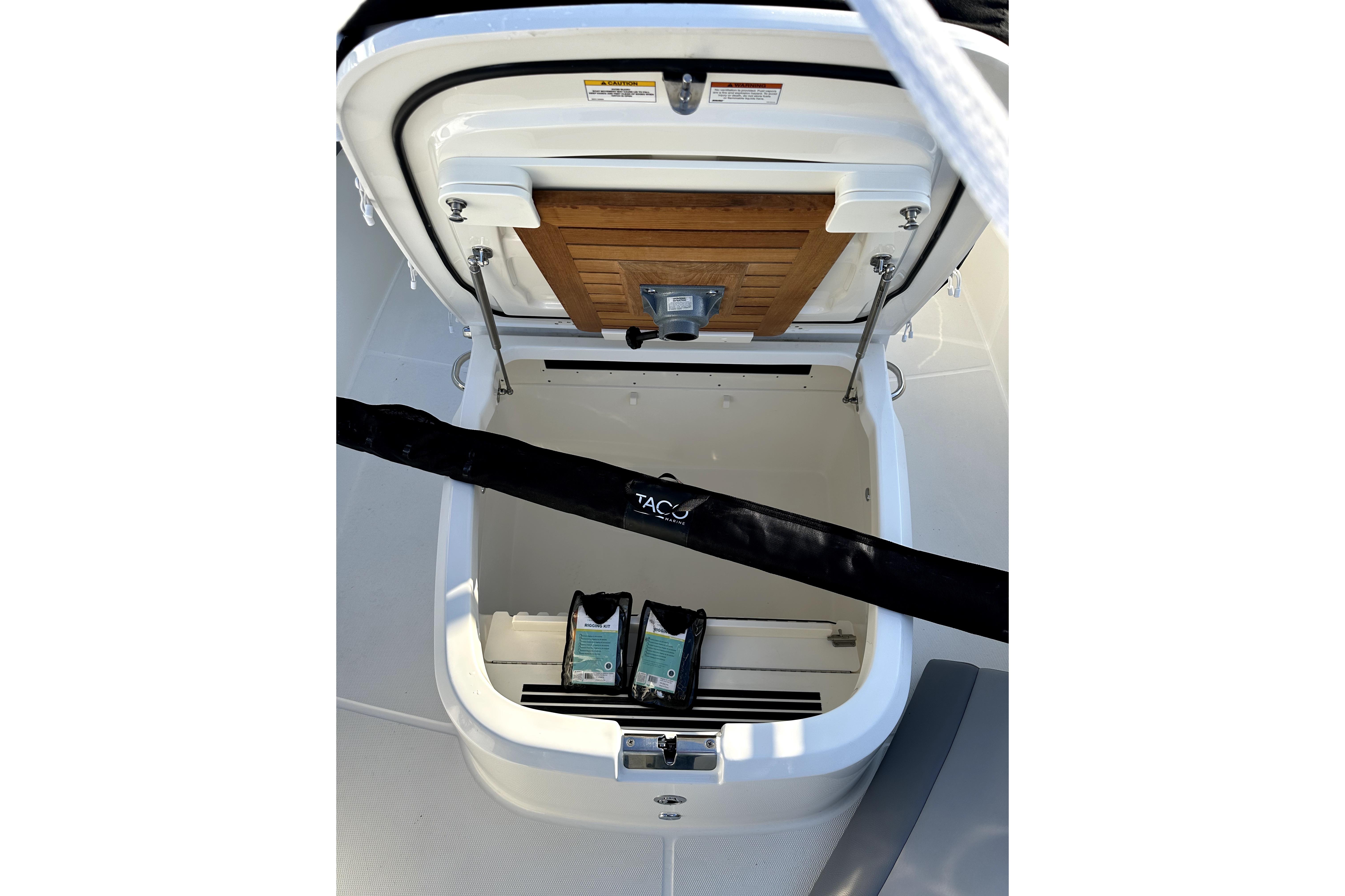 Open storage compartment on 2023 Boston Whaler OUTRAGE boat, featuring wooden panel and accessories.