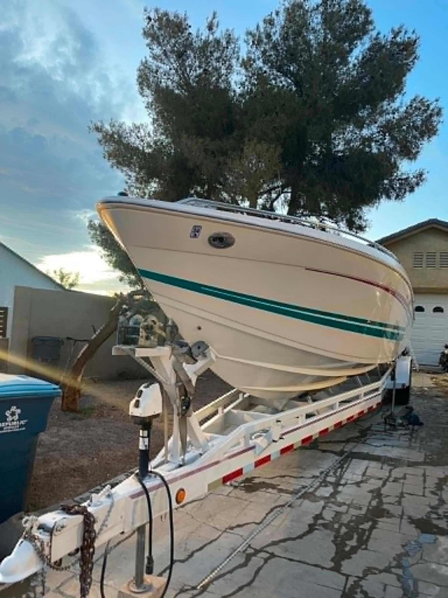 A white speedboat on a trailer, parked on a driveway, with trees in the background.