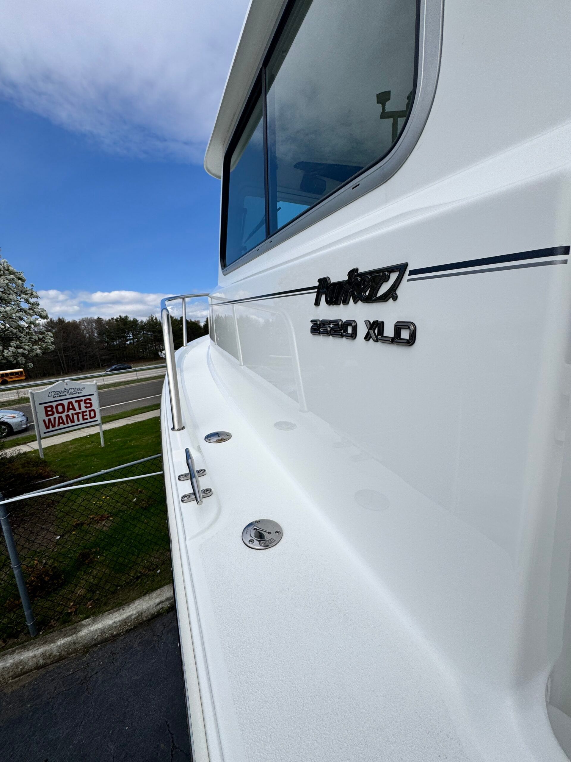Side view of a boat with a white hull and windows, "Boats Wanted" sign in the background.