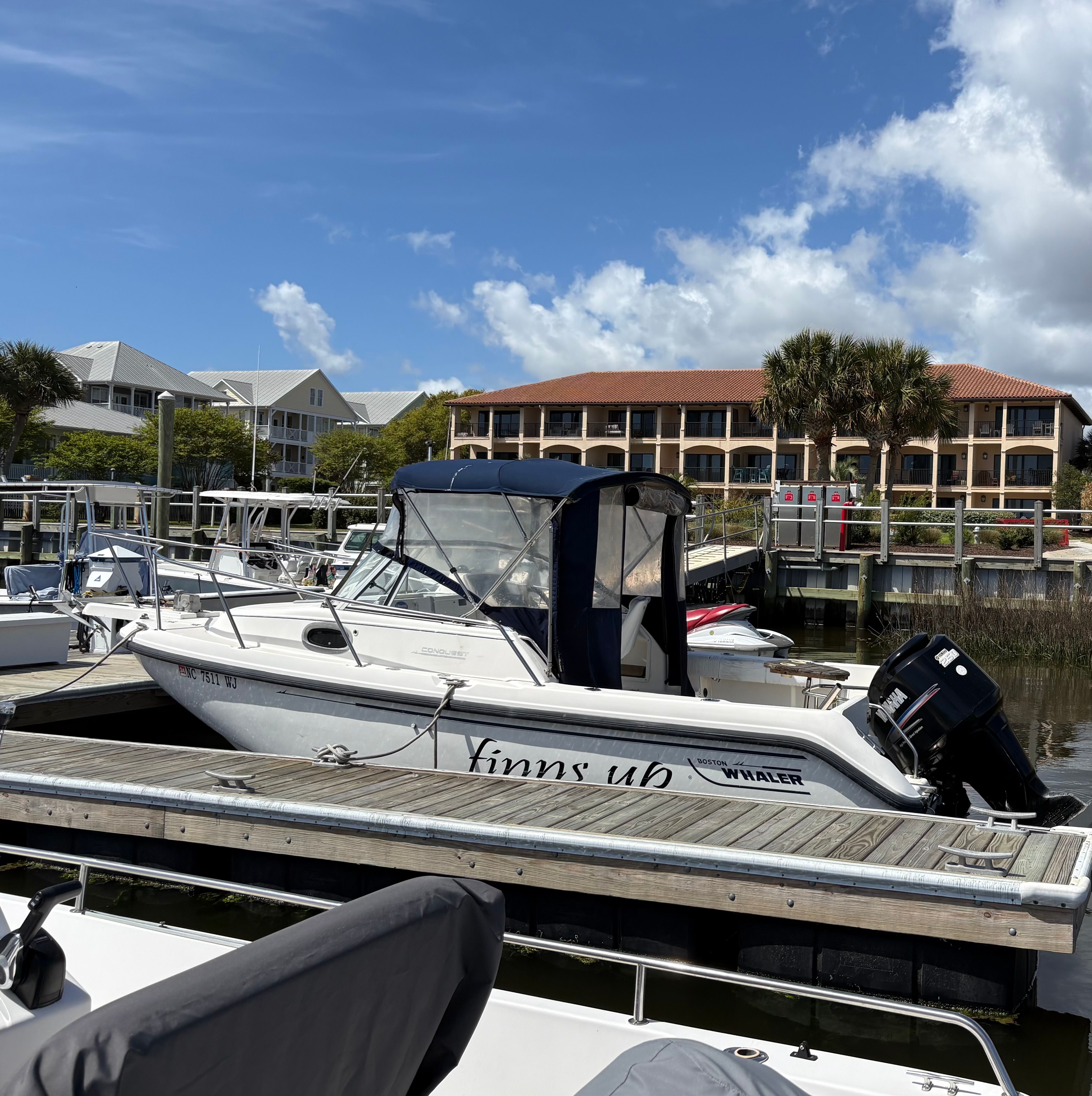 A 1999 Boston Whaler Conquest 21 docked on a sunny day with buildings in the background.