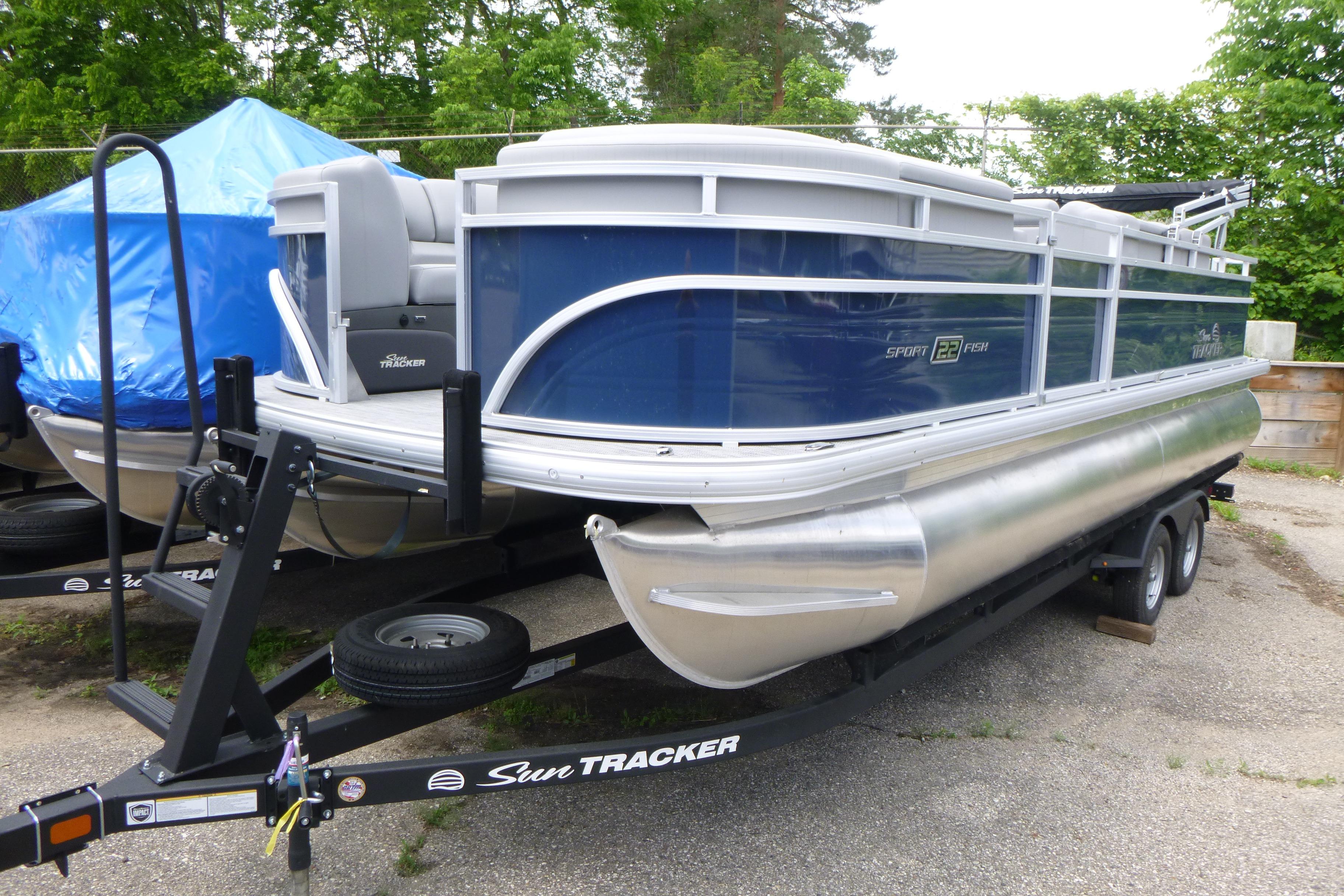 2026 Sun Tracker SportFish 22 DLX pontoon boat on trailer, parked outdoors.