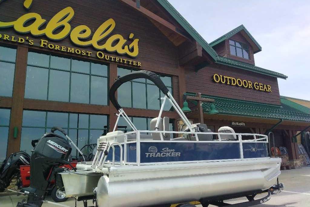 2026 Sun Tracker Bass Buggy 16 XL Select pontoon boat outside Cabela's outdoor gear store.