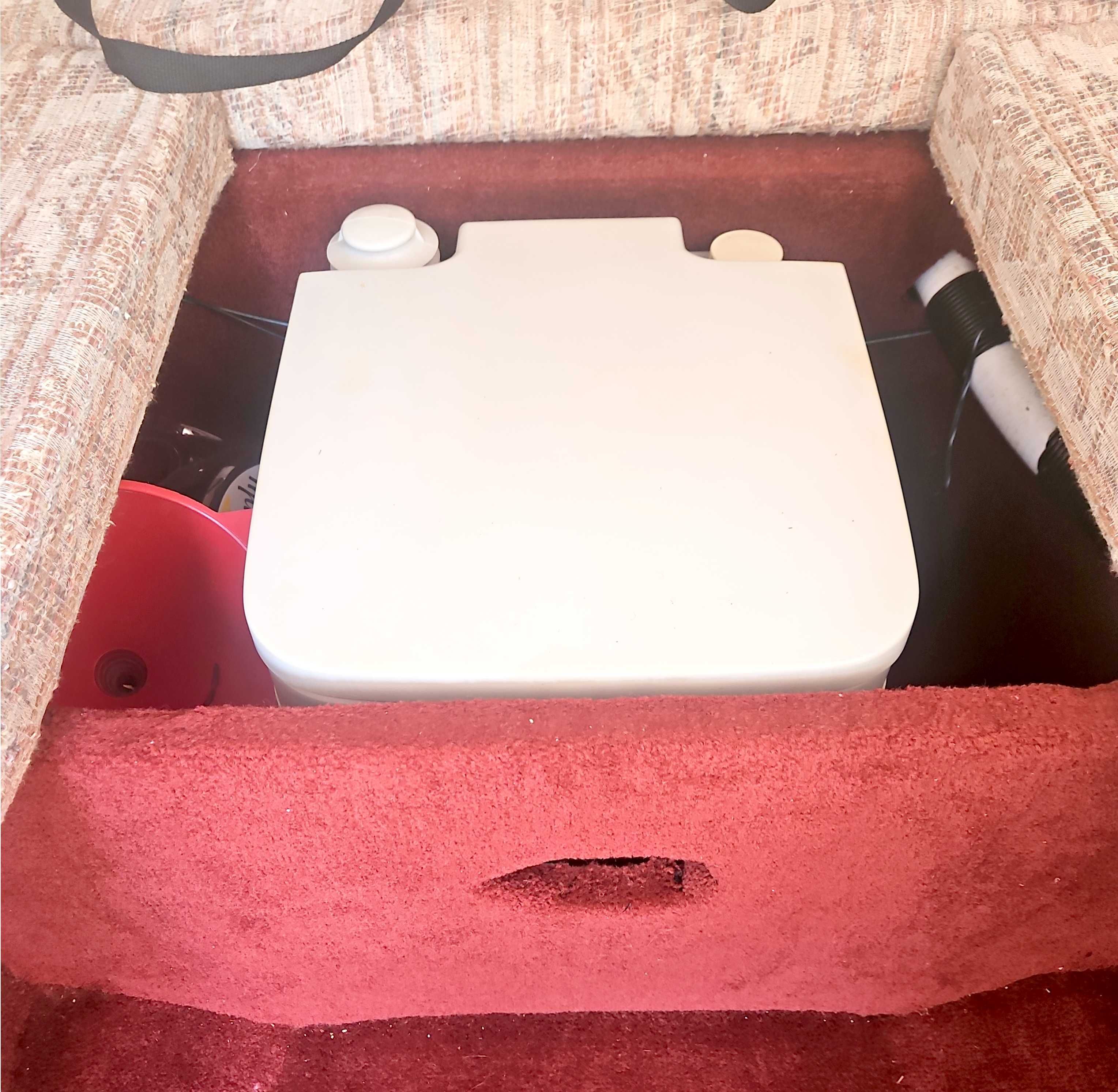 A white container is set into a red carpeted floor, surrounded by beige upholstery.