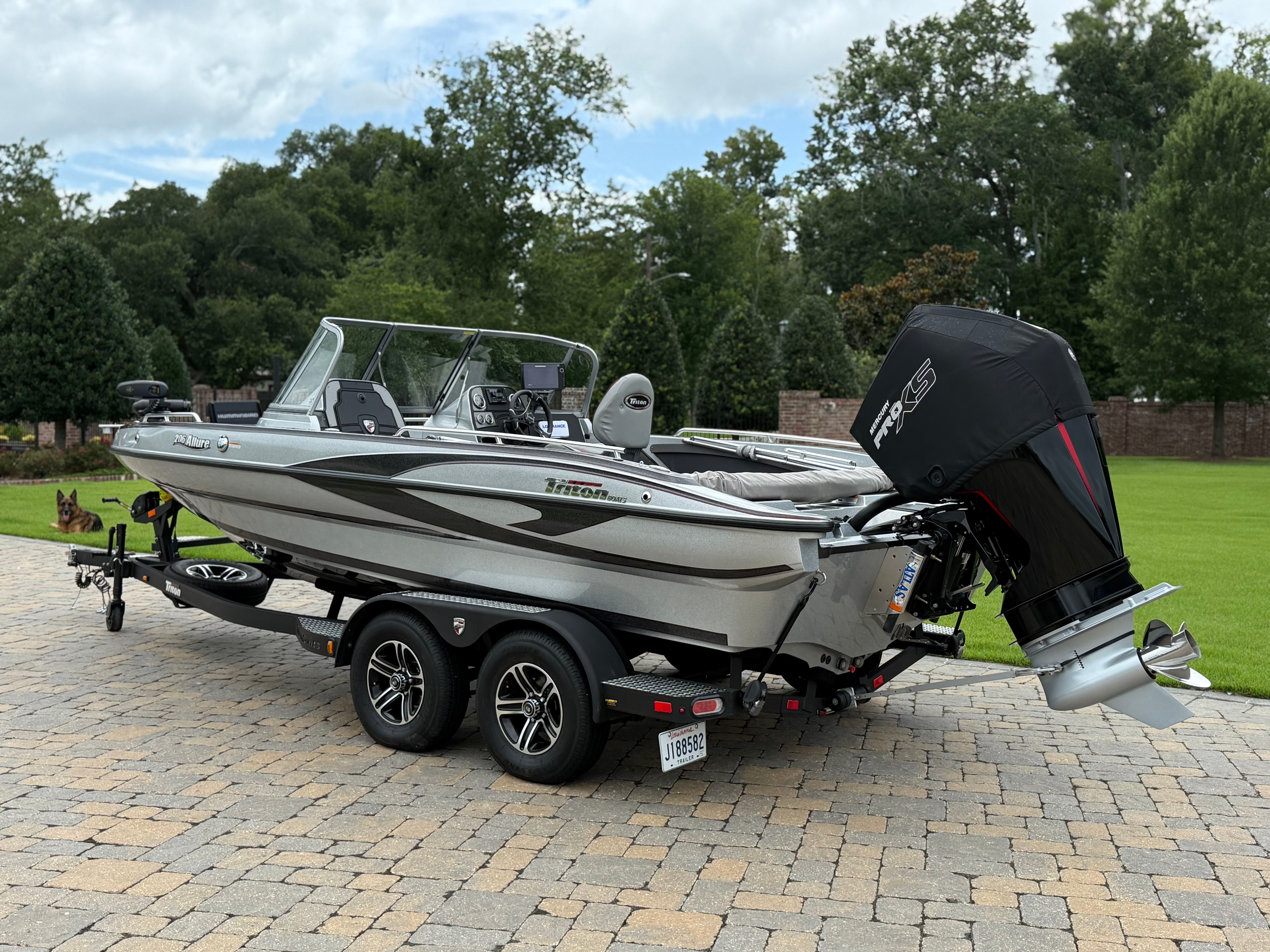 A silver 2023 Triton 206 Allure boat on a trailer in a paved yard.