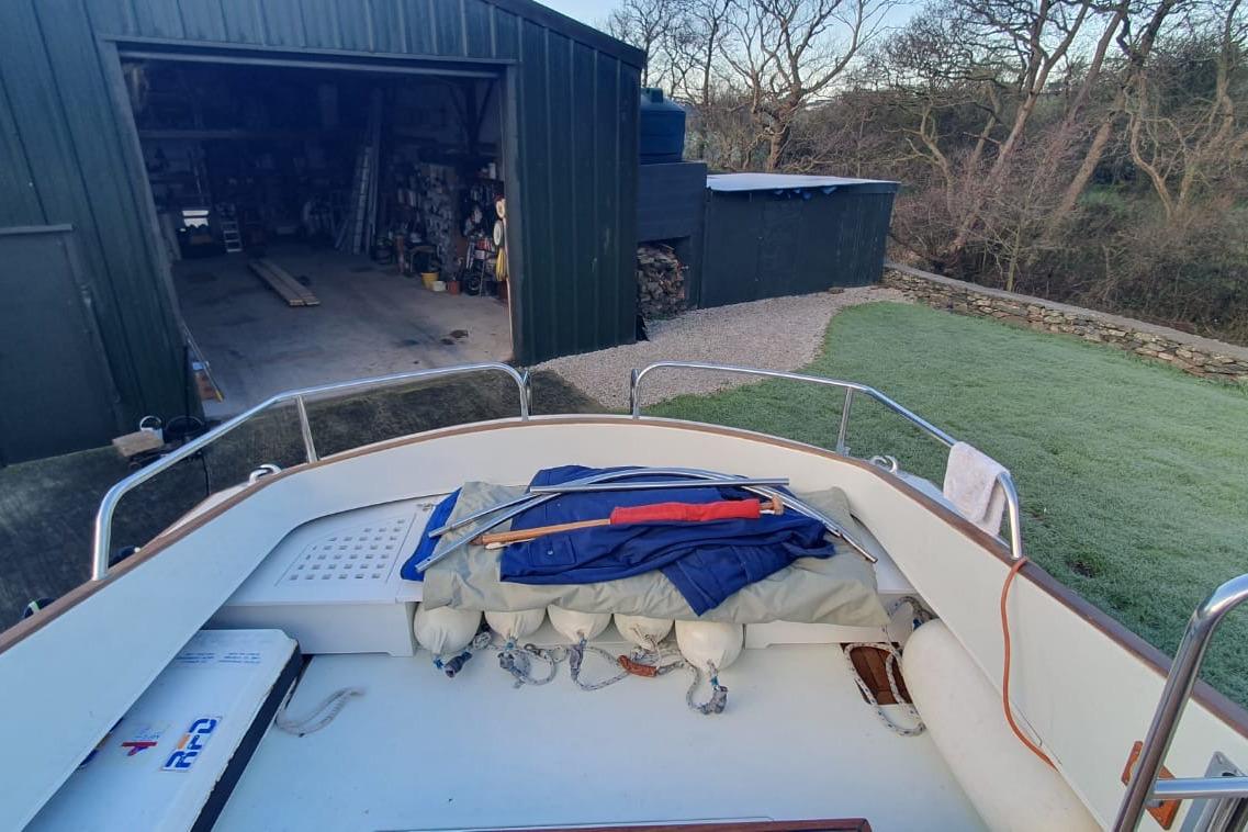 1989 Fairey Spearfish MKIII boat docked near a garage, surrounded by trees.